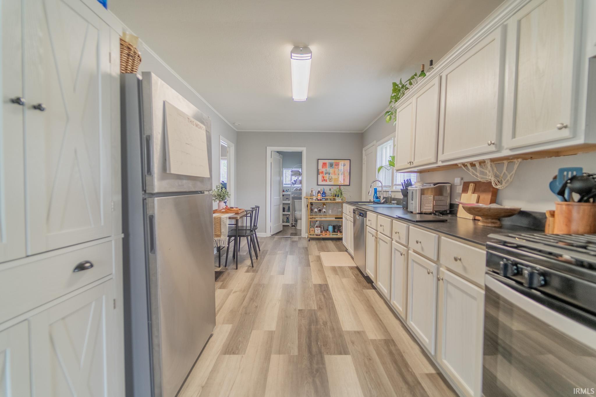 Galley kitchen featuring wood-finish flooring, white cabinetry, dark countertops, and stainless steel appliances
