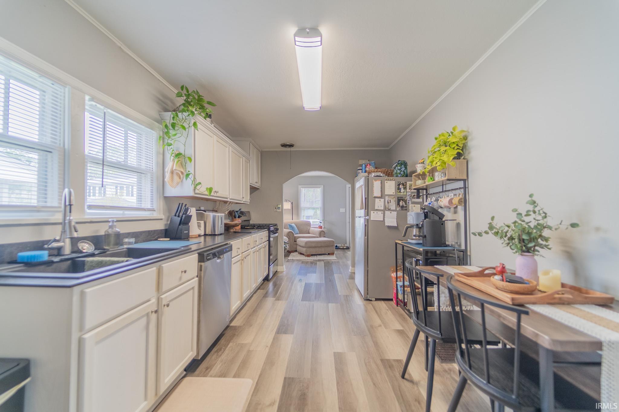 Galley kitchen featuring white cabinetry, dark countertops, wood-finish flooring, two windows with blinds, and stainless steel appliances