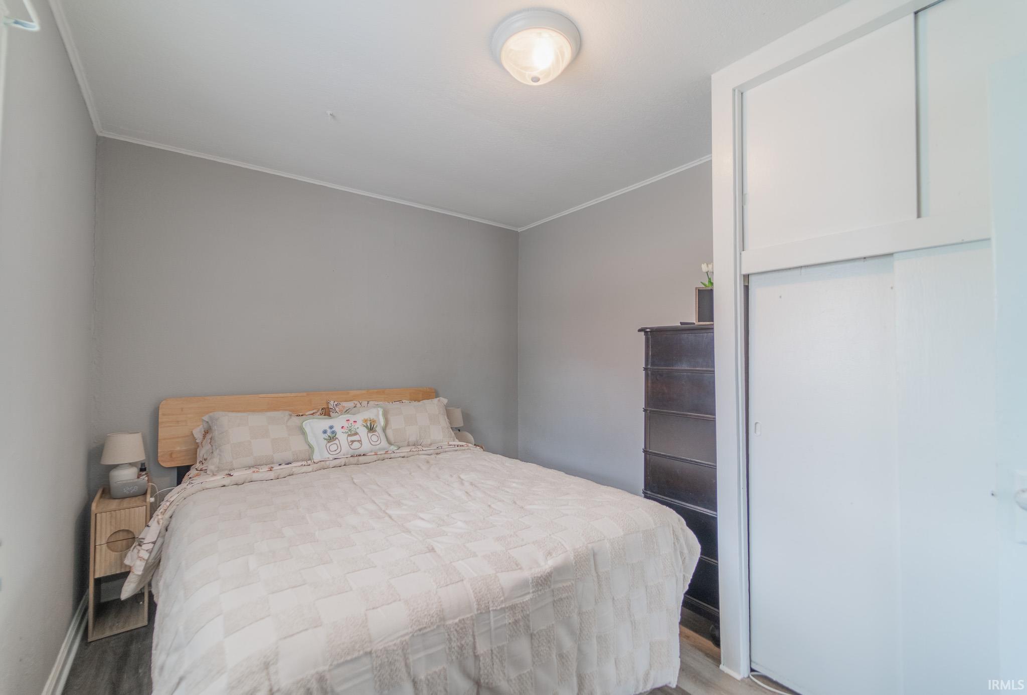 Bedroom featuring a light wood-finish headboard, gray wall paint, wood-finish flooring, and a built-in closet with sliding white doors