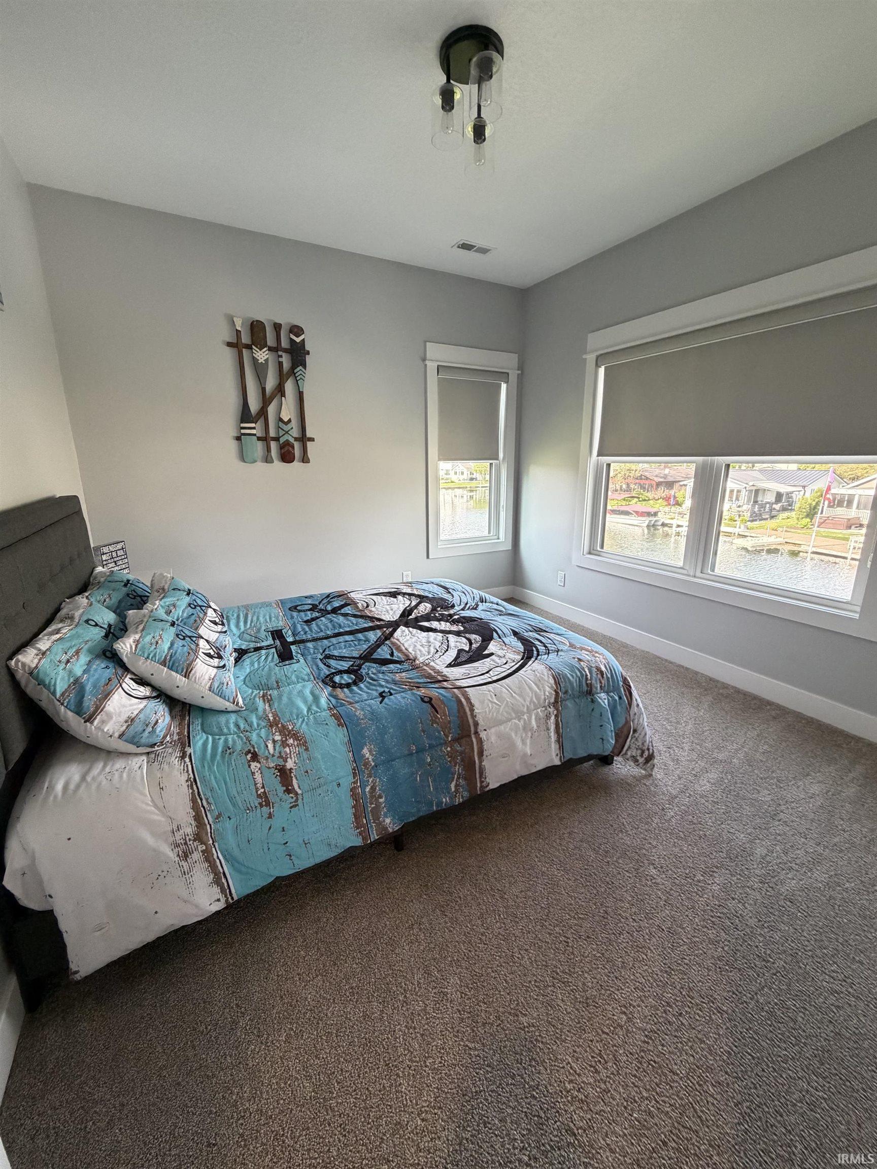 Bright interior space featuring two windows with roller shades, a contemporary flush mount light fixture, and neutral carpeting