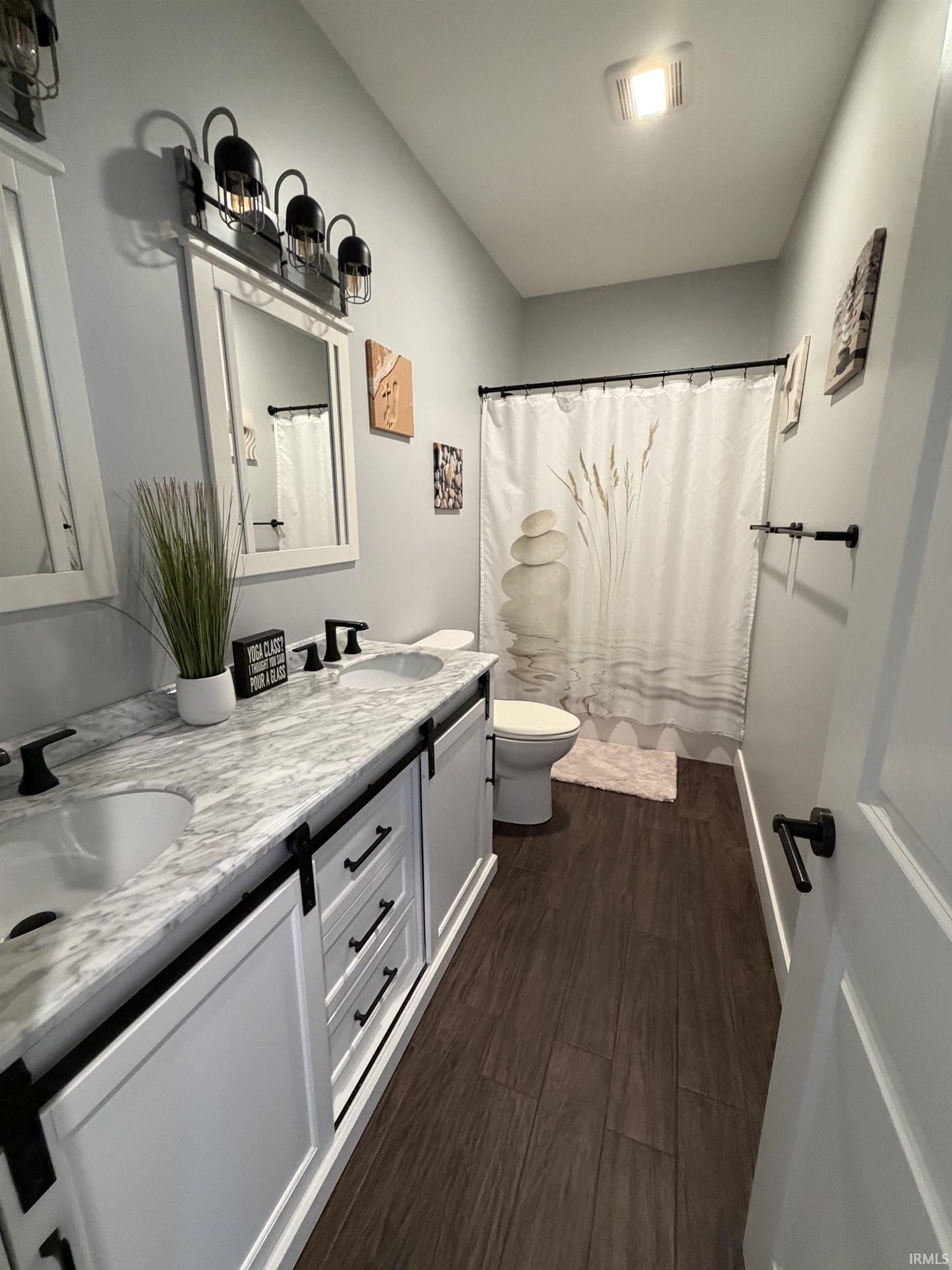 Bathroom featuring a double vanity with stone-finish countertop, dual undermount sinks, and dark wood-finish flooring