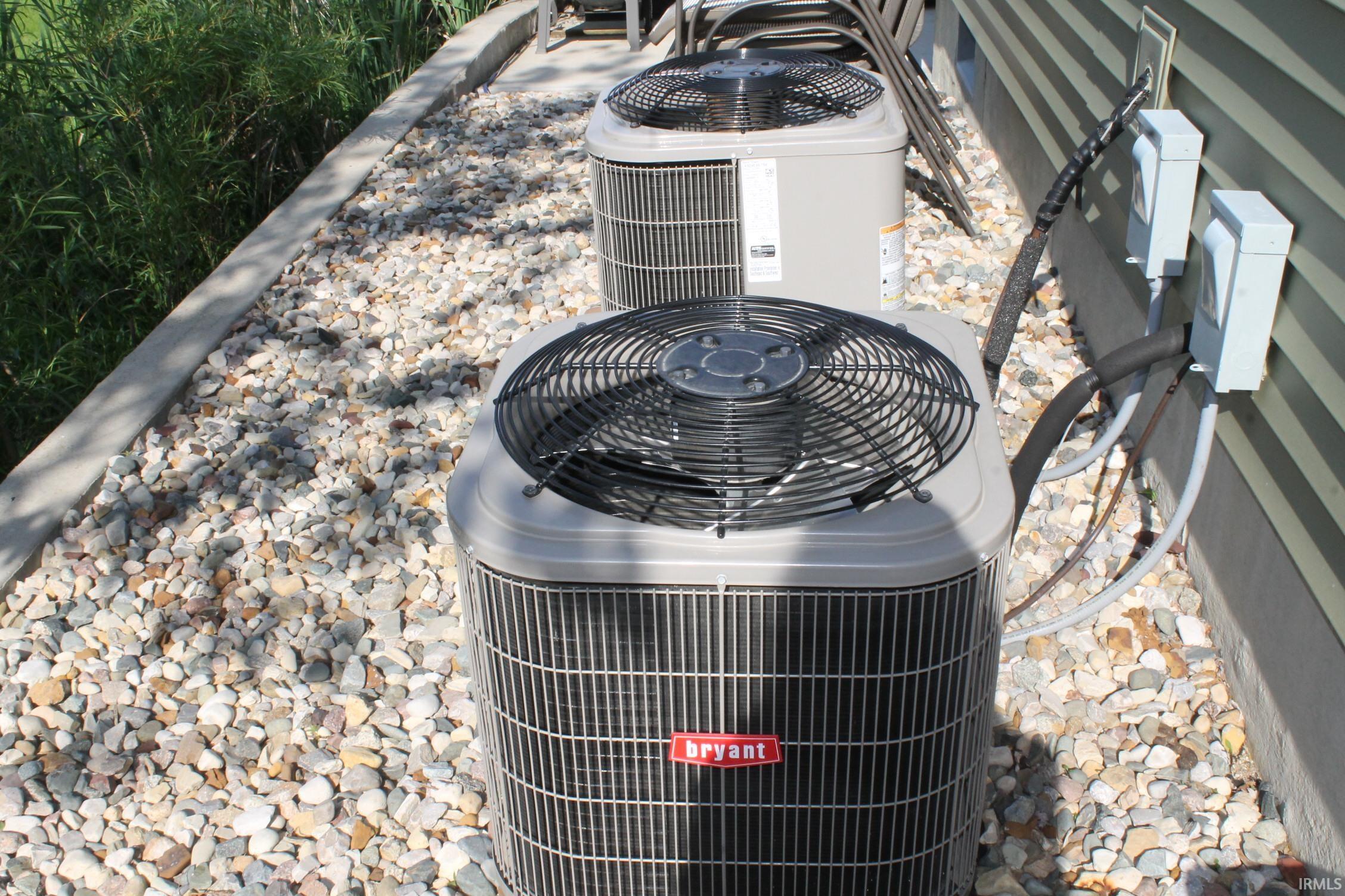 Dual exterior HVAC units on a gravel bed with a concrete retaining wall