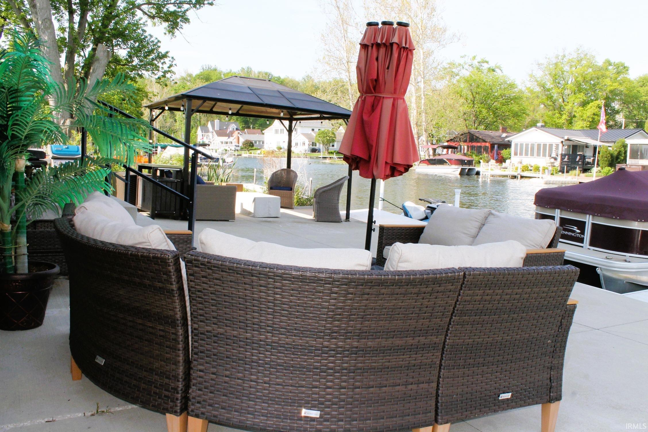 Expansive waterfront patio featuring a permanent gazebo structure, concrete hardscaping, and direct water access with a dock