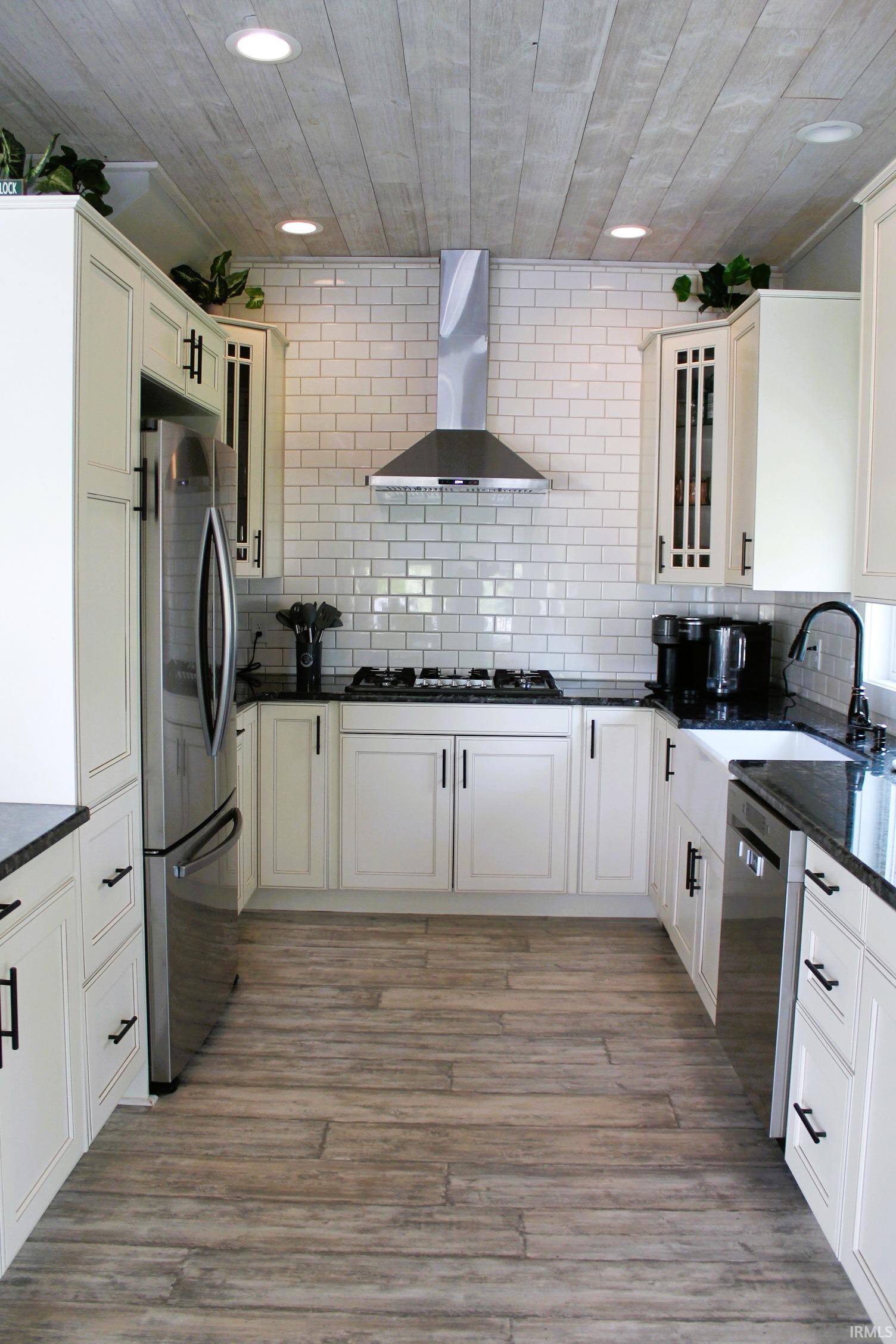 U-shaped kitchen featuring white shaker cabinetry, dark countertops, a subway tile backsplash, stainless steel appliances, and wood-finish flooring