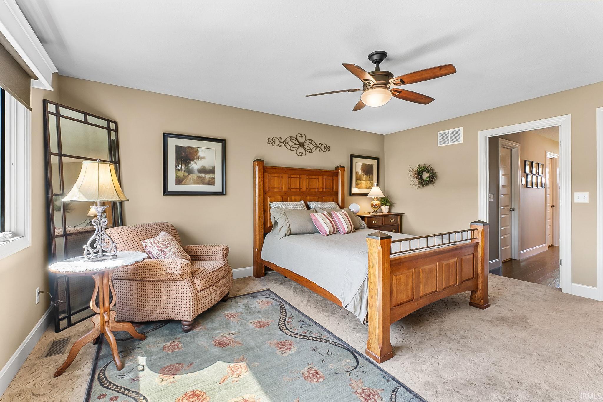 Spacious bedroom featuring light-colored carpeting, a ceiling fan with integrated lighting, and a large window with roller shades