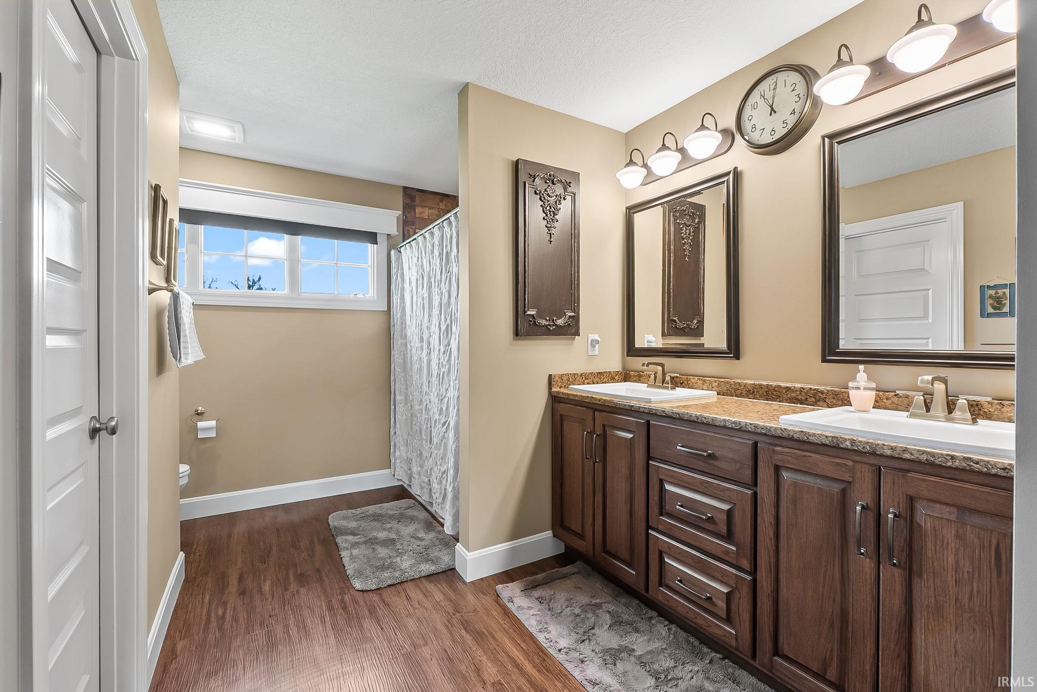 Bathroom featuring a dual vanity with wood-finish cabinetry, a stone-finish countertop, and individual framed mirrors