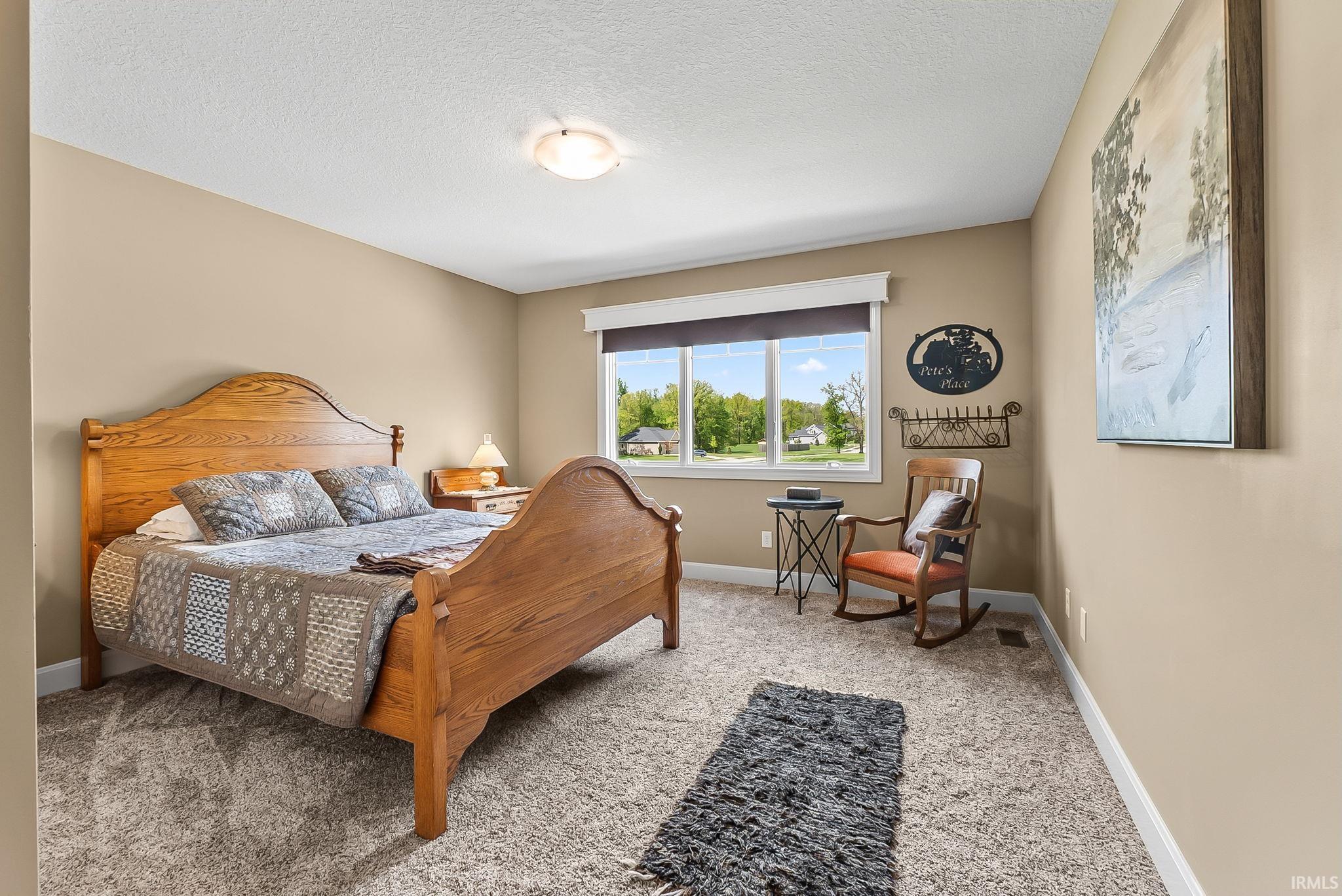 Carpeted bedroom featuring neutral wall tones, a large window with white trim, and a flush-mount ceiling light fixture