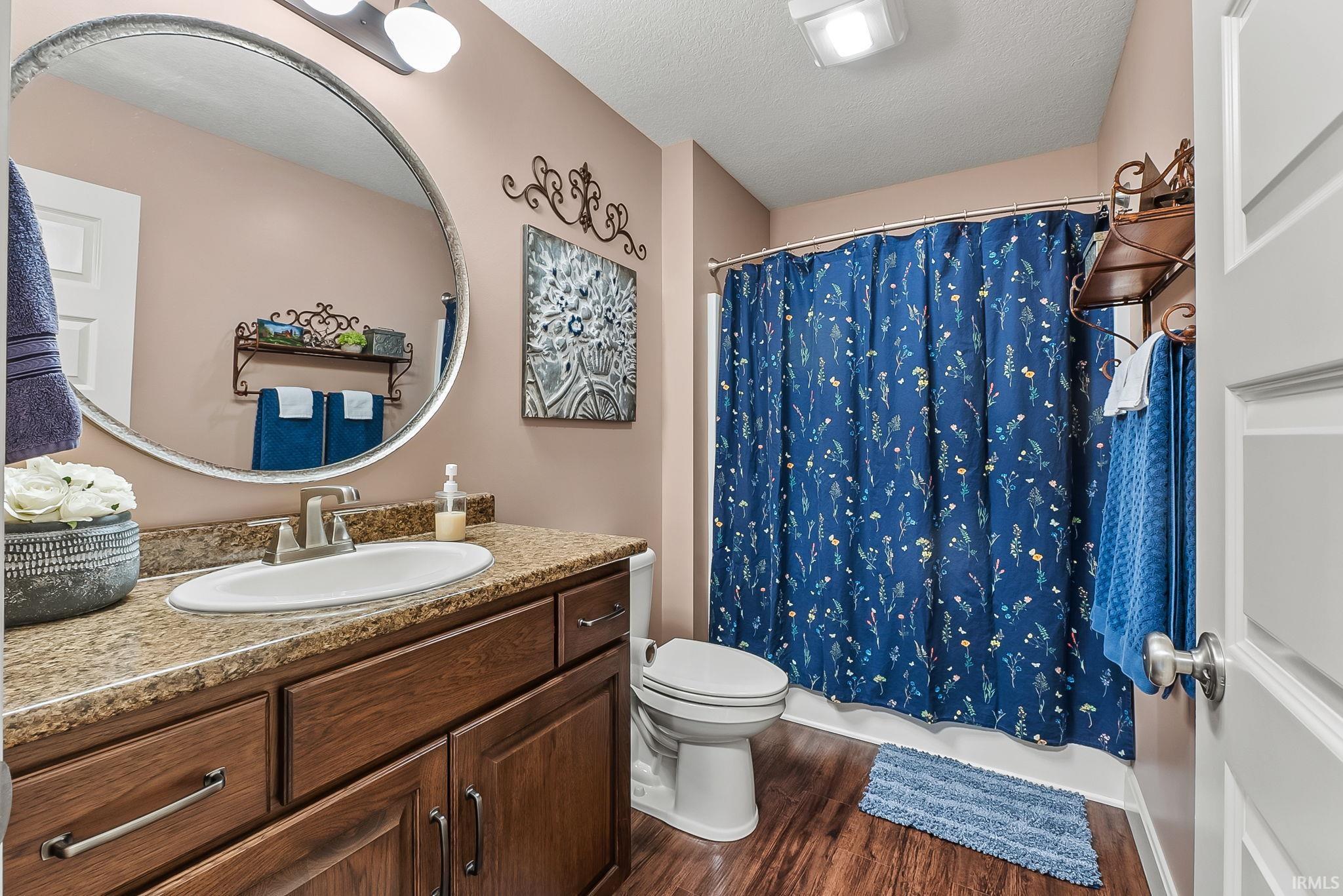 Bathroom featuring a wood-finish vanity with an undermount sink, a countertop, a wall-mounted mirror, and a shower with a curtain rod
