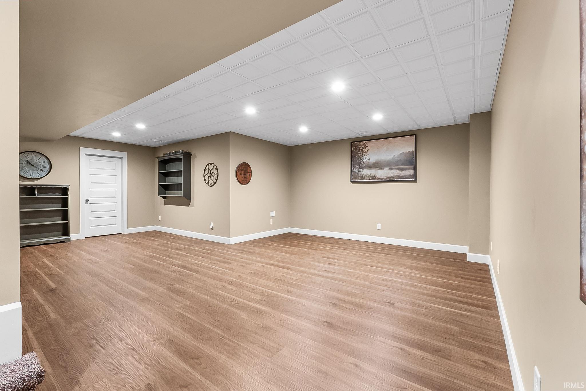 Spacious room featuring wood-finish flooring, recessed lighting, neutral paint, white baseboards, and a white panel door