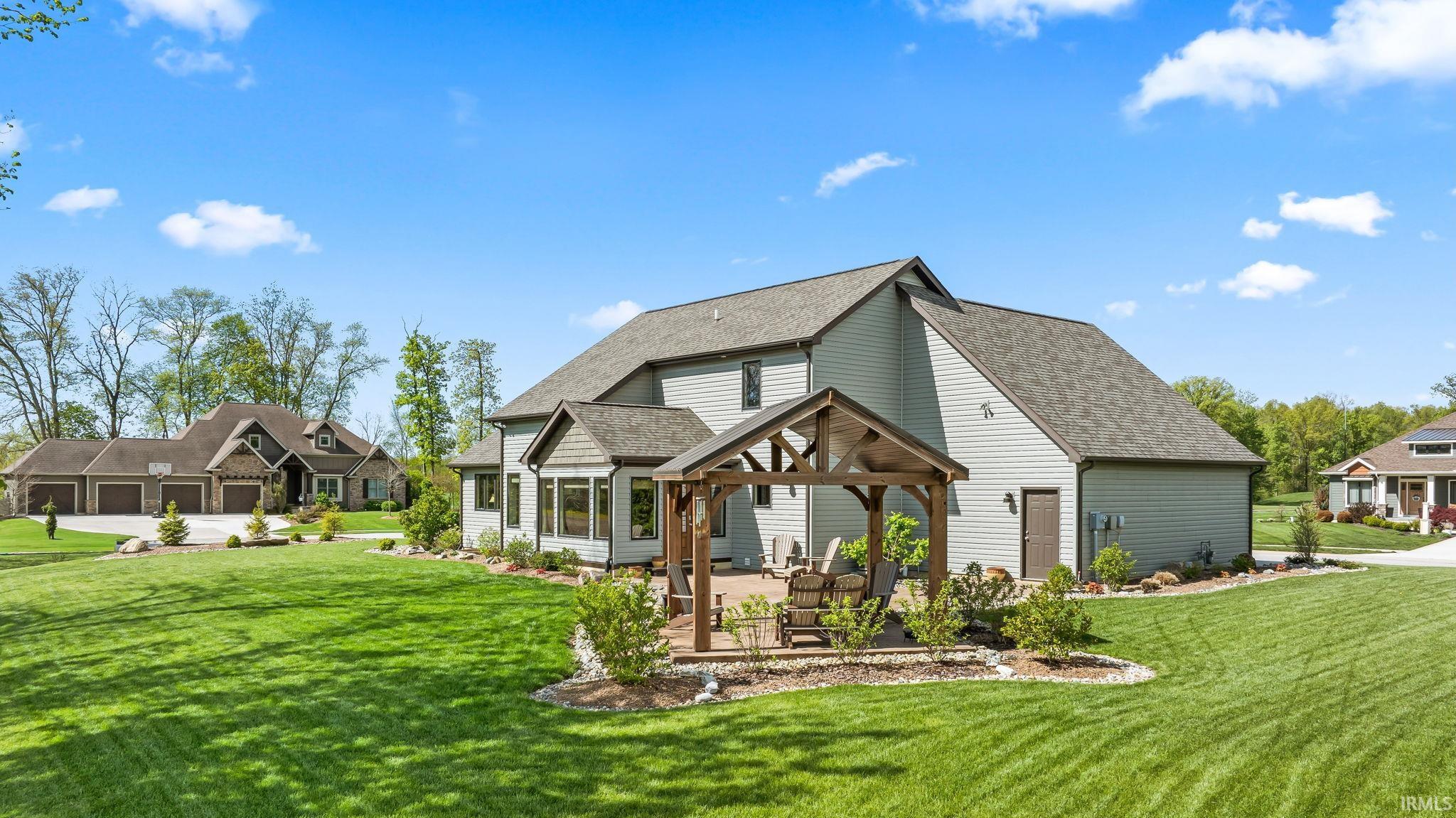 Spacious backyard featuring a large green lawn, a stone patio with a wood-frame pergola, and mature landscaping