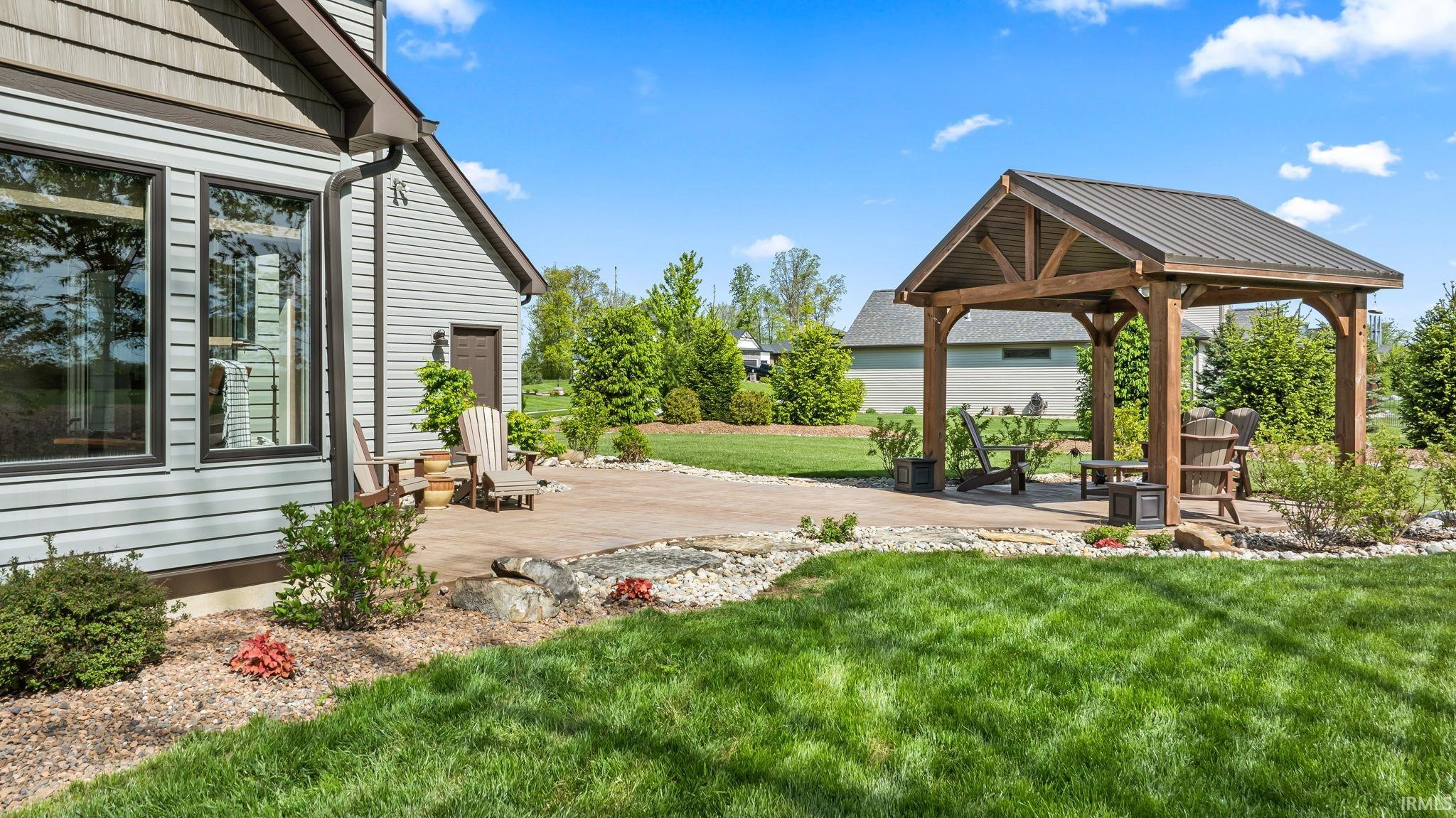 Expansive backyard featuring a natural wood pergola with a metal roof, a spacious hardscaped patio, and a manicured lawn