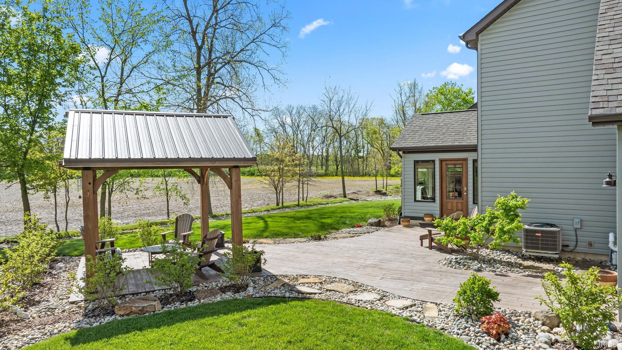 Expansive outdoor living area featuring a wood-framed pergola with a metal roof, a spacious stamped concrete patio, and lush green lawn areas