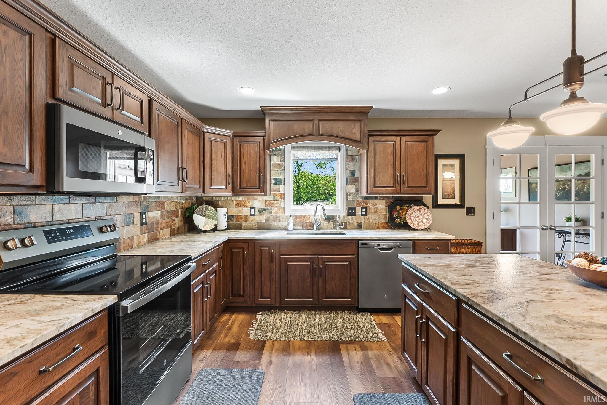 Kitchen featuring wood-finish cabinetry, stainless steel appliances, stone-look countertops, a tiled backsplash, and wood-finish flooring