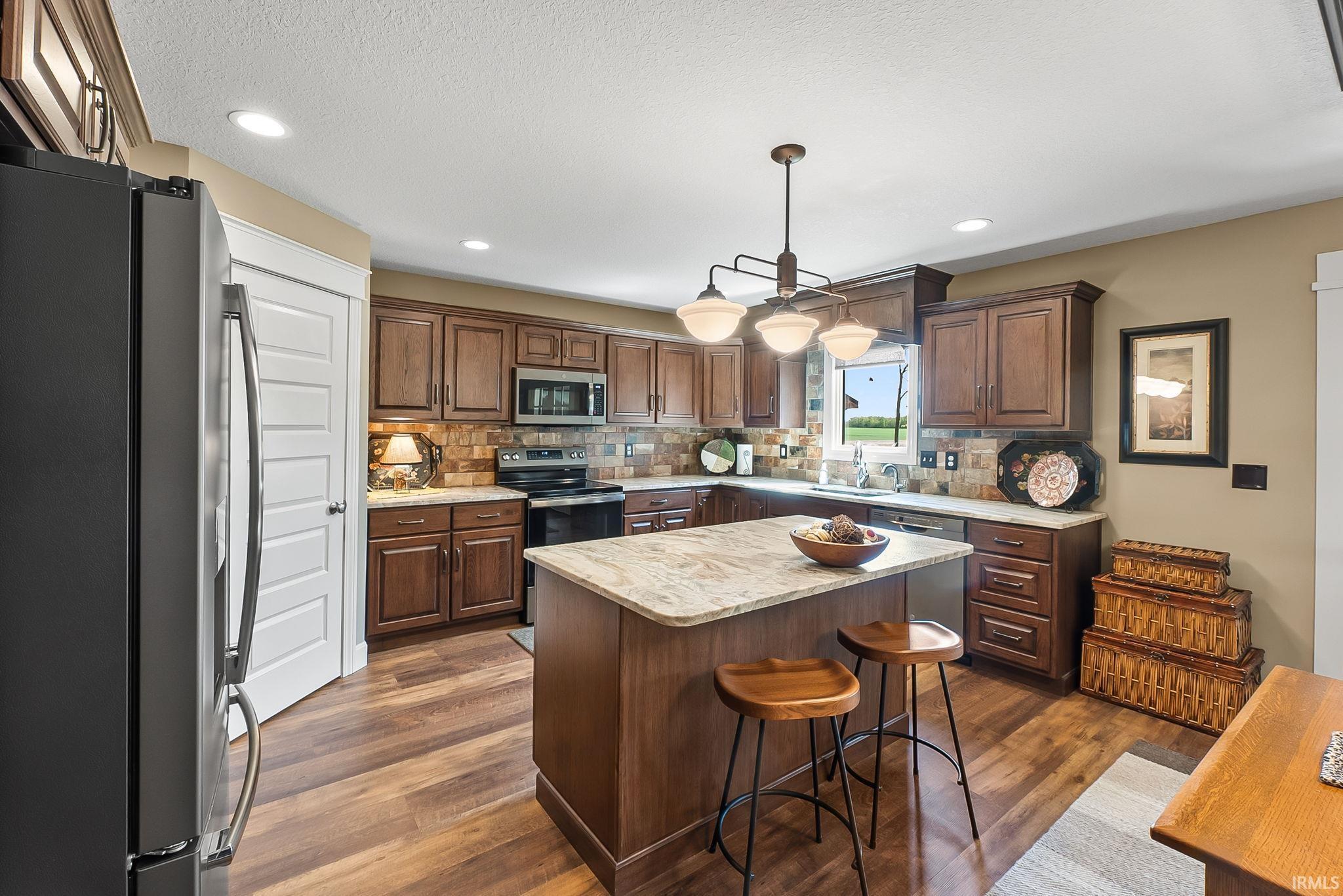 Kitchen featuring wood-finish flooring, dark wood cabinetry, a central island with a light-toned countertop, and a tile backsplash