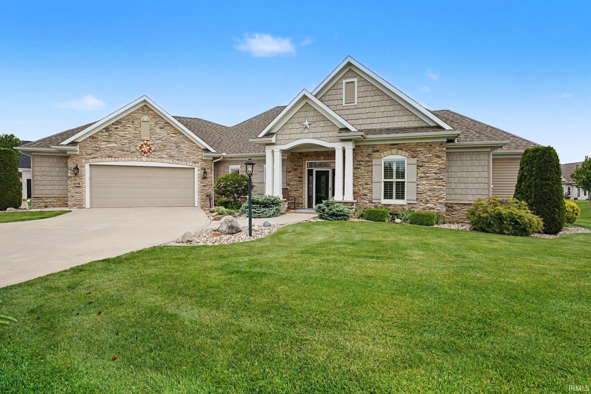 Stone and shake-sided ranch-style residence featuring a two-car garage, covered entry with columns, arched window with shutters, and established perimeter landscaping