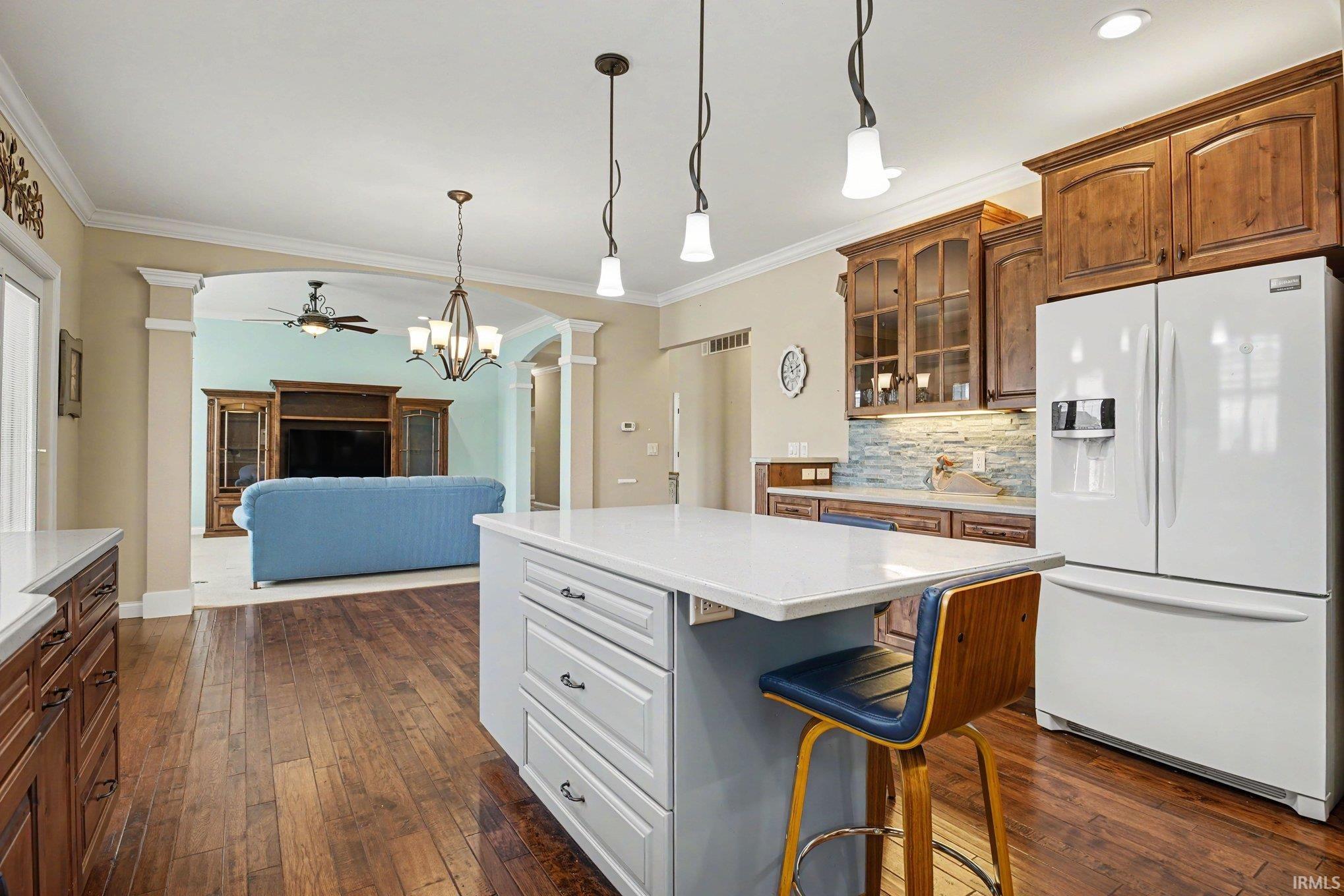 Kitchen featuring a central island with white countertop, pendant lighting, and rich wood-finish flooring