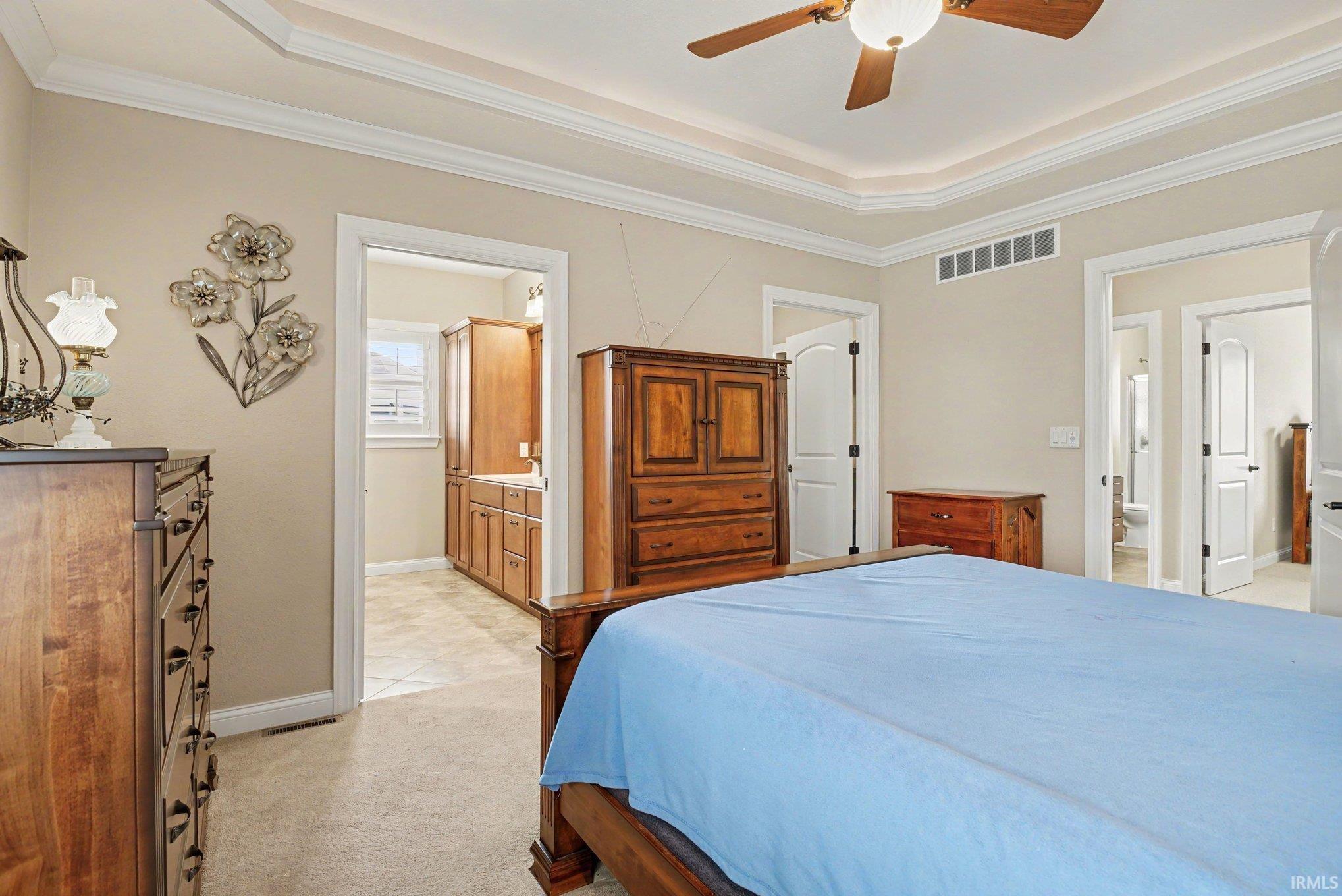 Recessed tray ceiling with crown molding, carpeted flooring, and a ceiling fan with integrated lighting