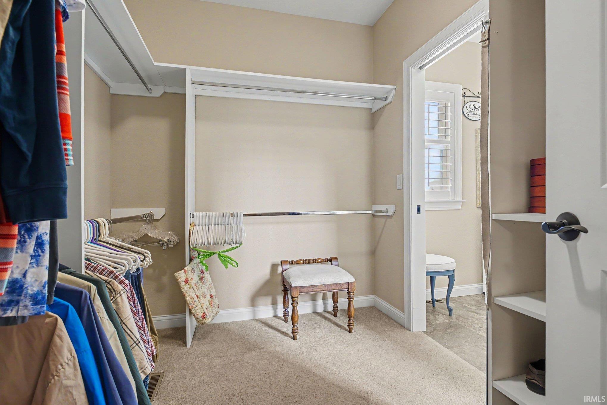 Walk-in closet featuring carpet flooring, built-in shelving, hanging rods, and an interior window with plantation shutters