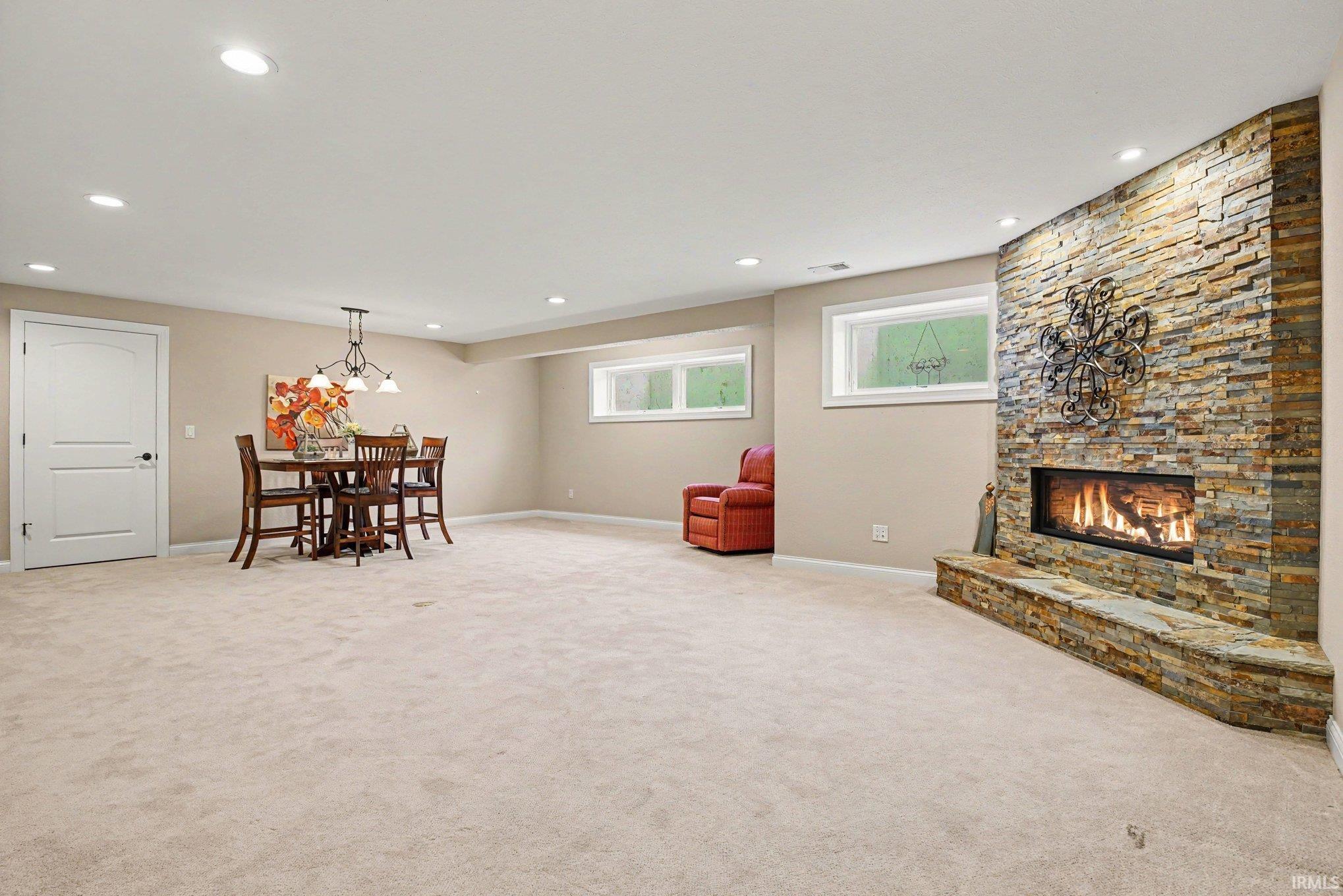 Spacious room featuring a stacked stone fireplace with a stone hearth, recessed lighting, and light-colored carpeting