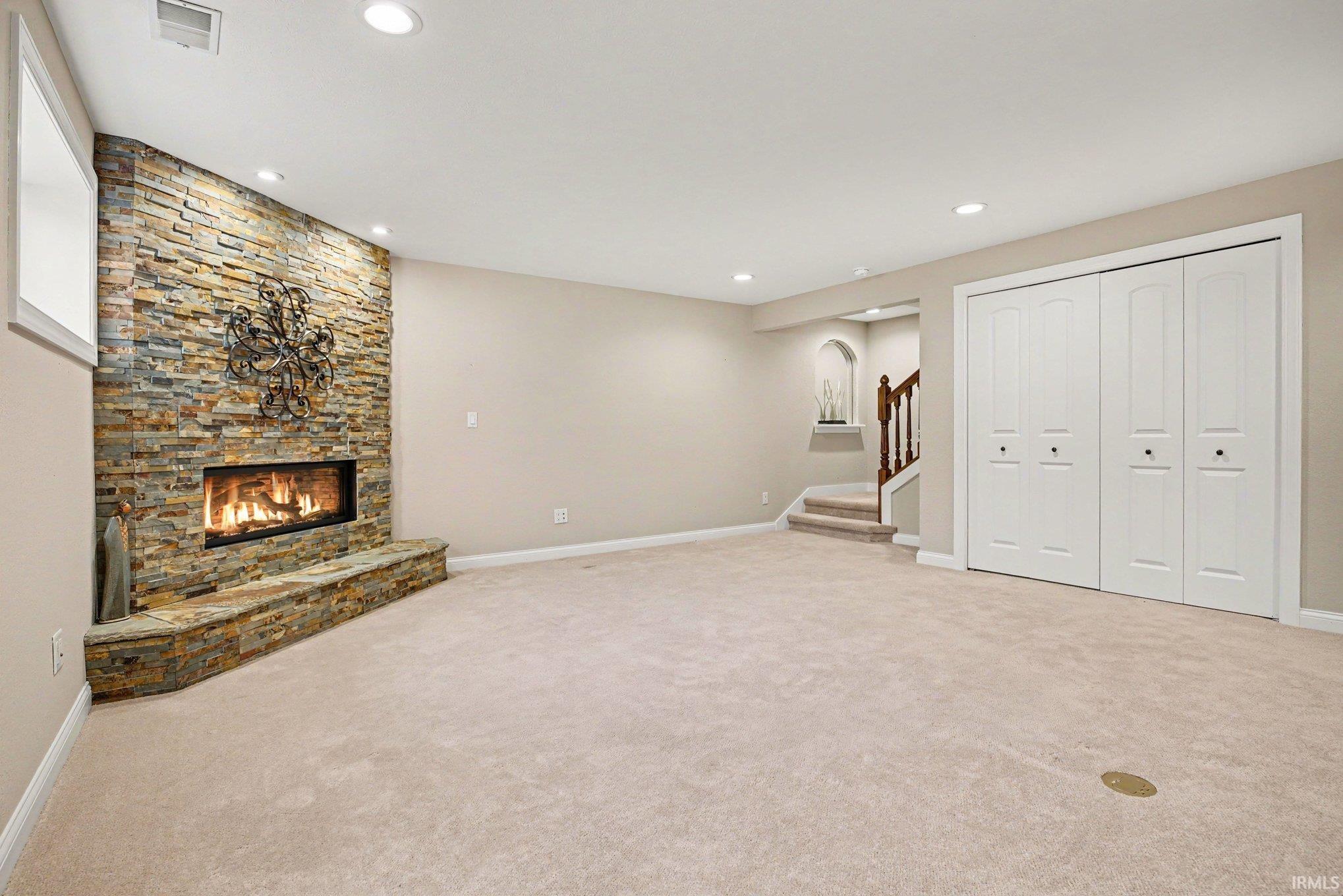 Spacious room featuring a stacked stone fireplace with a stone hearth, recessed lighting, neutral carpeting, and white bi-fold closet doors