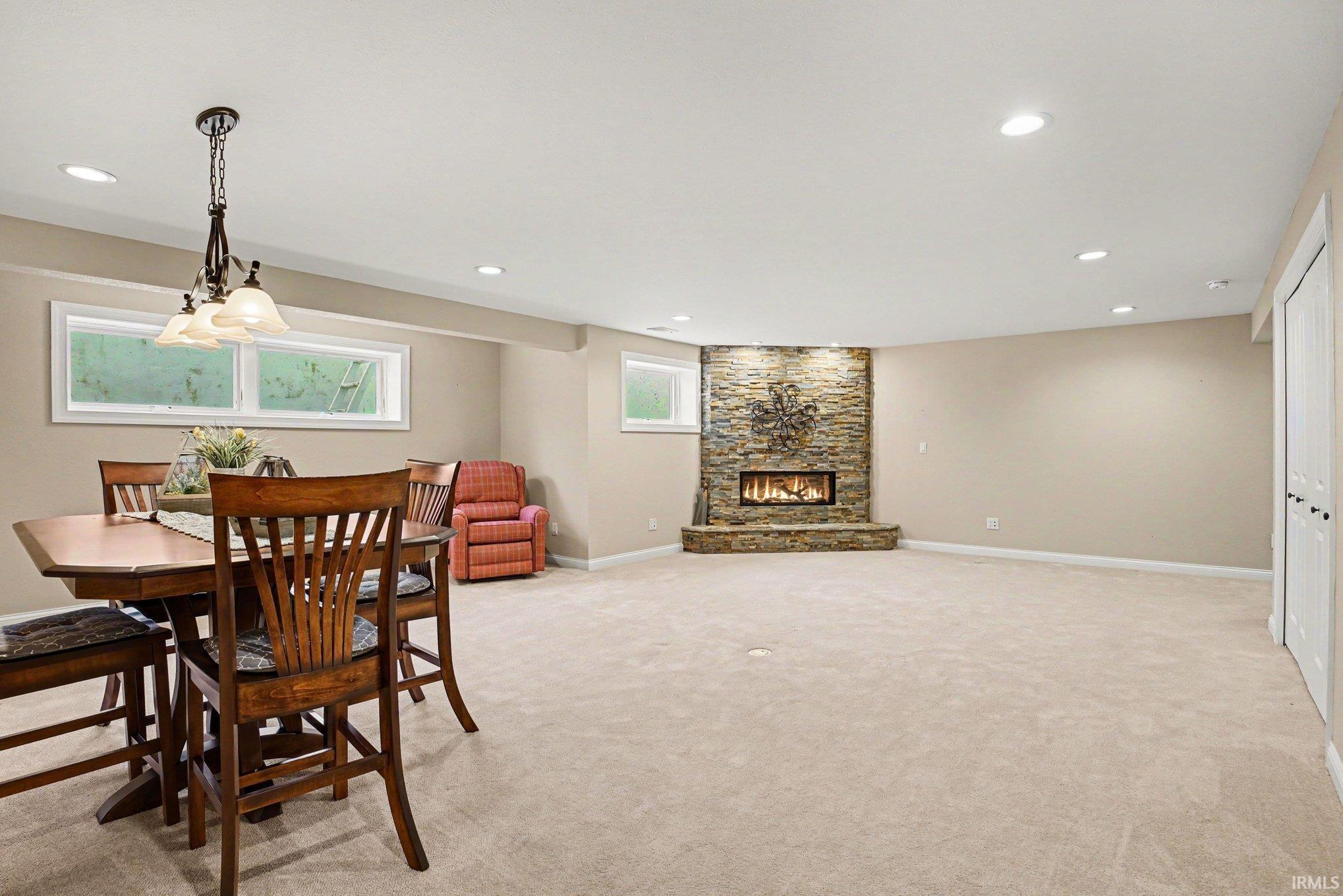 Spacious lower level featuring a stacked stone fireplace, recessed lighting, neutral carpet, and white trim