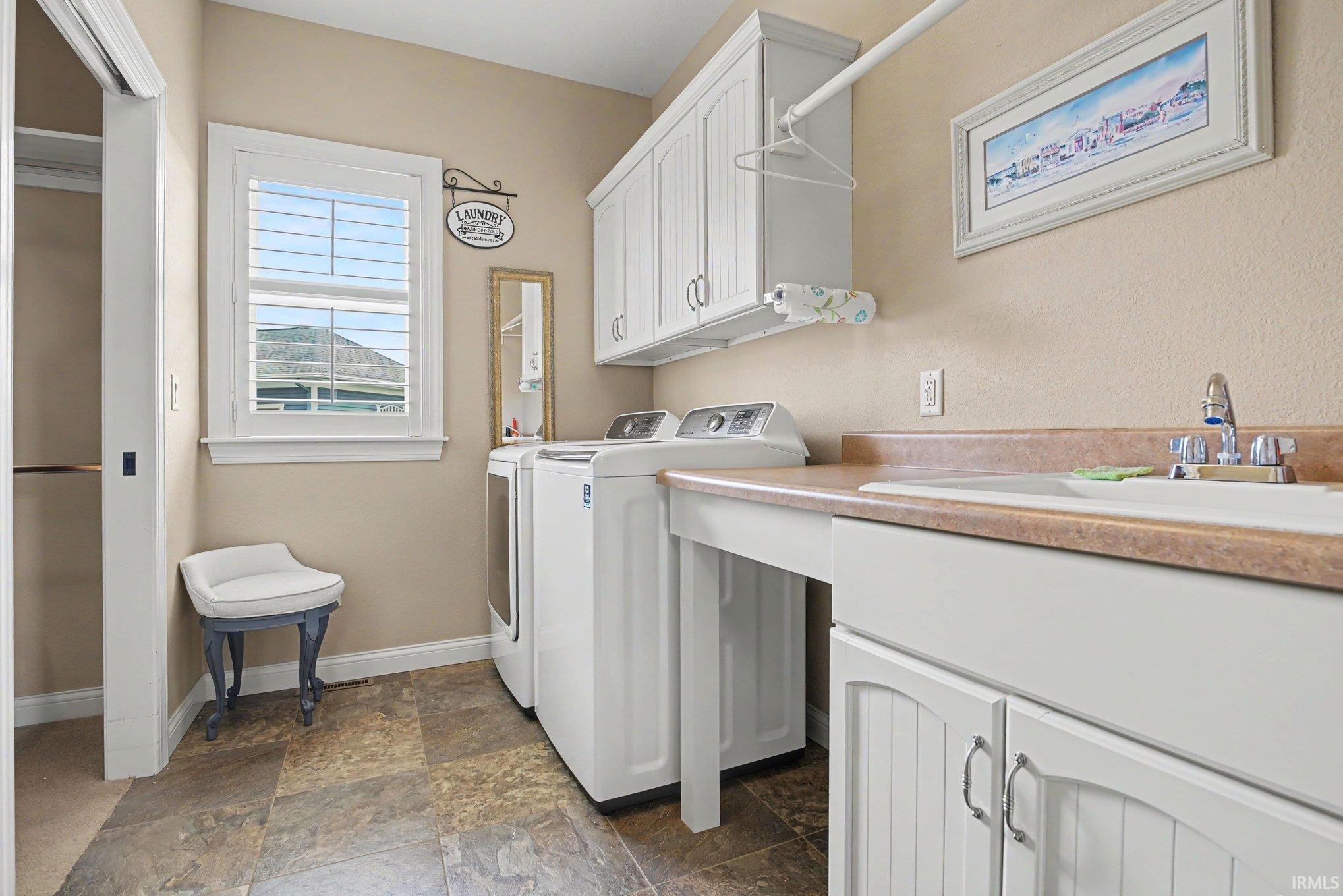 Dedicated laundry room featuring tile flooring, a window with plantation shutters, upper and lower cabinetry, a utility sink, and ample countertop space