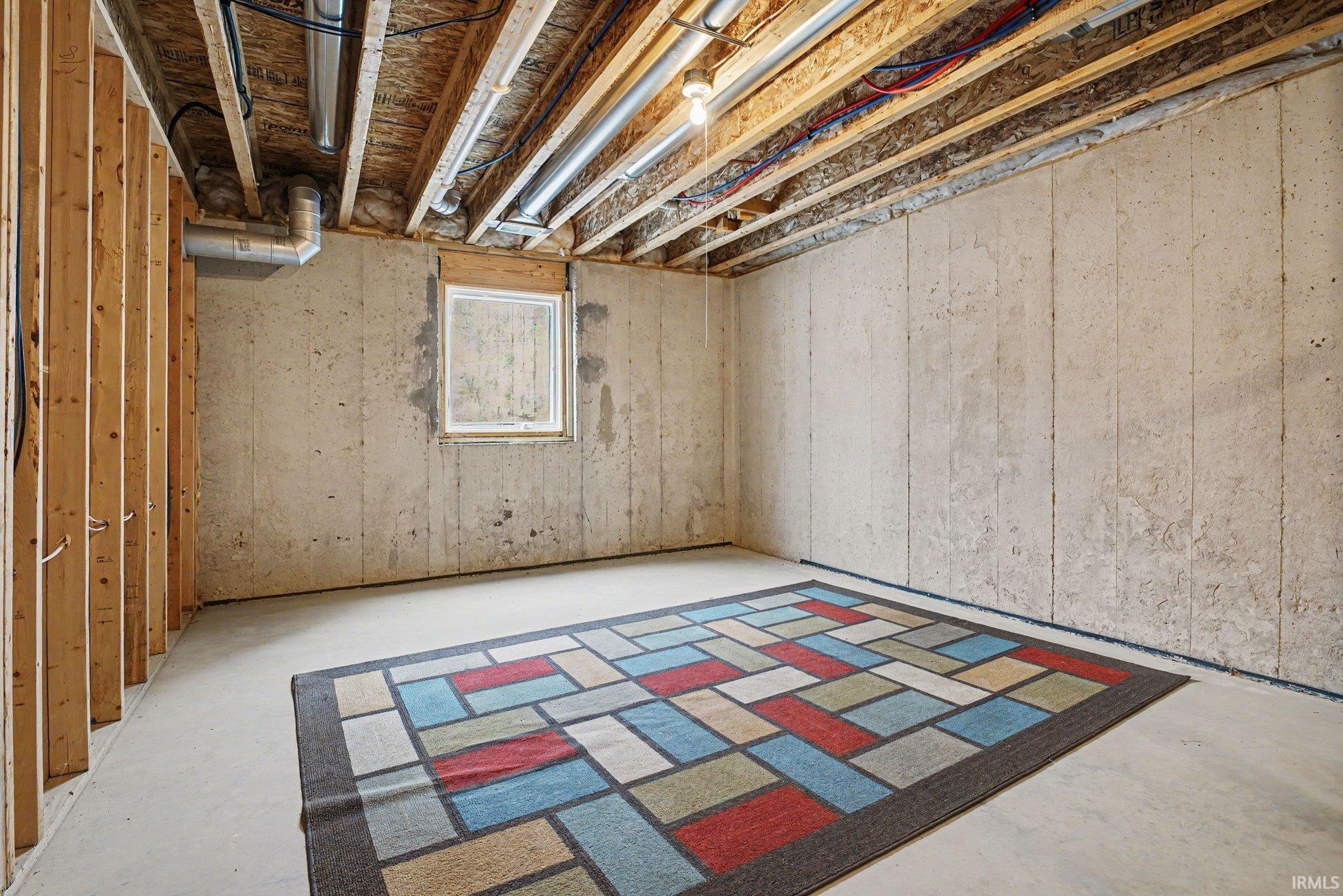 Unfinished lower level featuring exposed wood framing, concrete foundation walls, a single window, and exposed ceiling joists with visible utilities