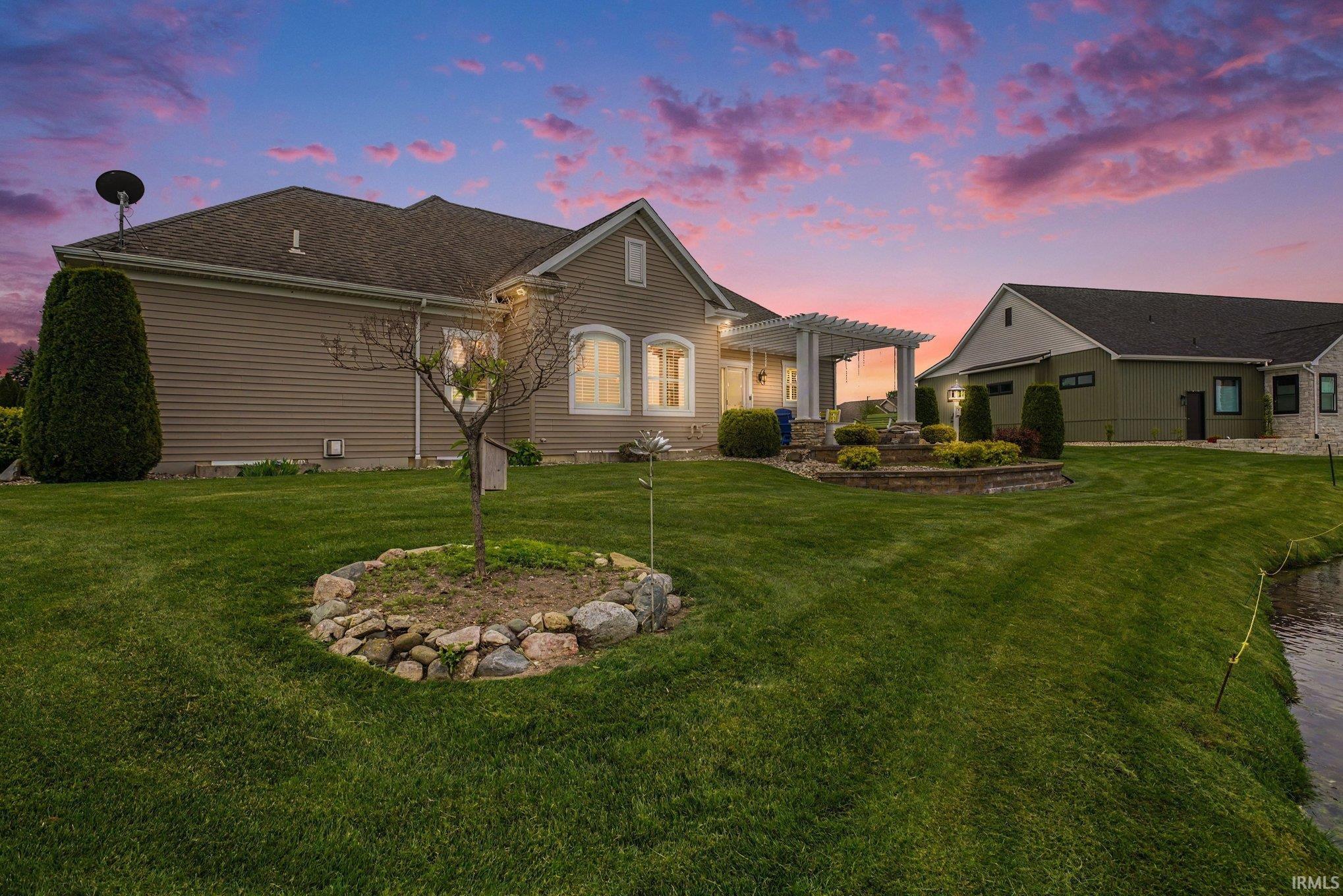 Expansive rear exterior featuring a covered patio with a white pergola, tiered landscaping, and an additional detached structure