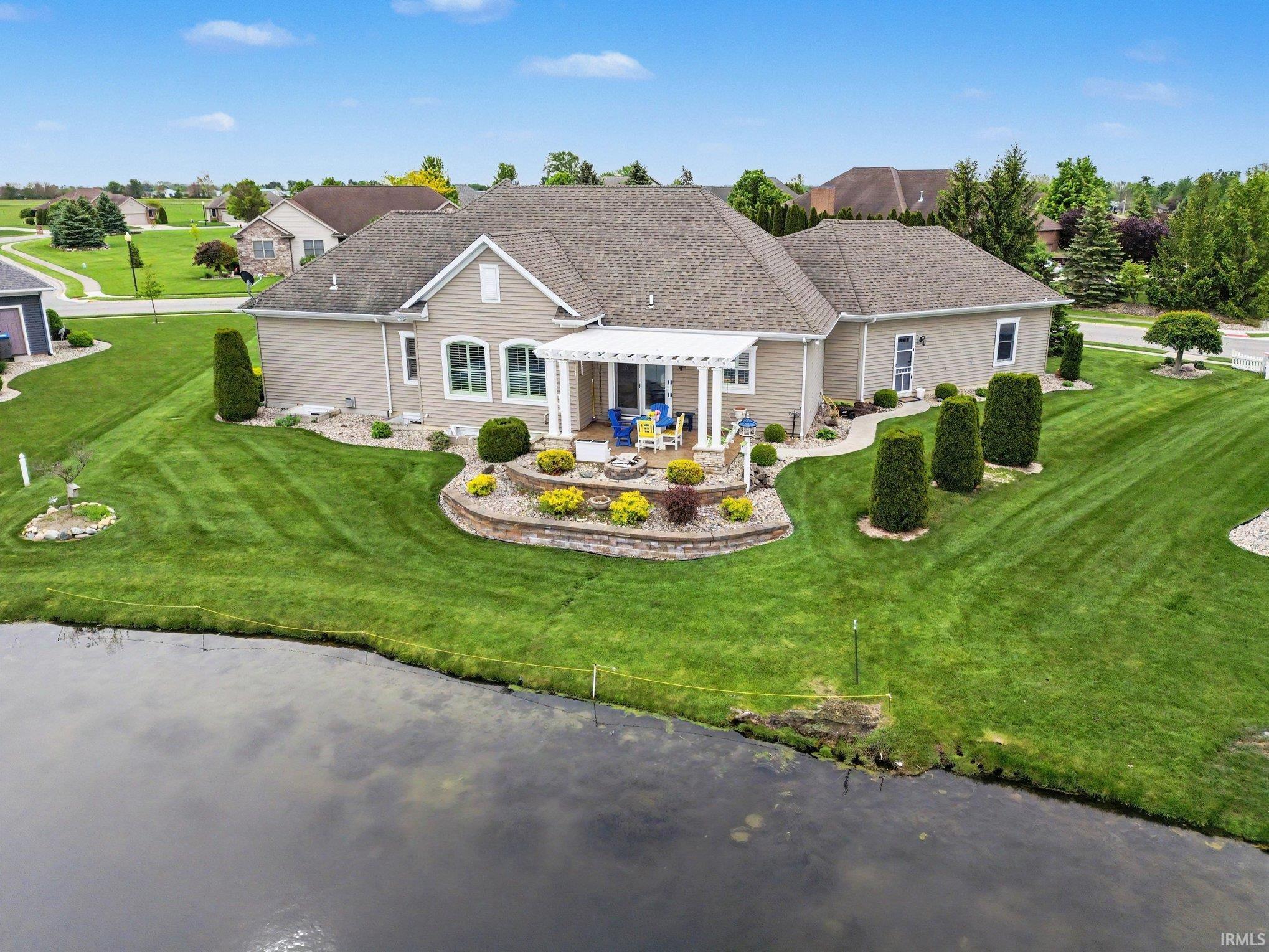 Expansive rear lawn featuring a tiered stone retaining wall with mature landscaping, a covered patio with a pergola, and water frontage