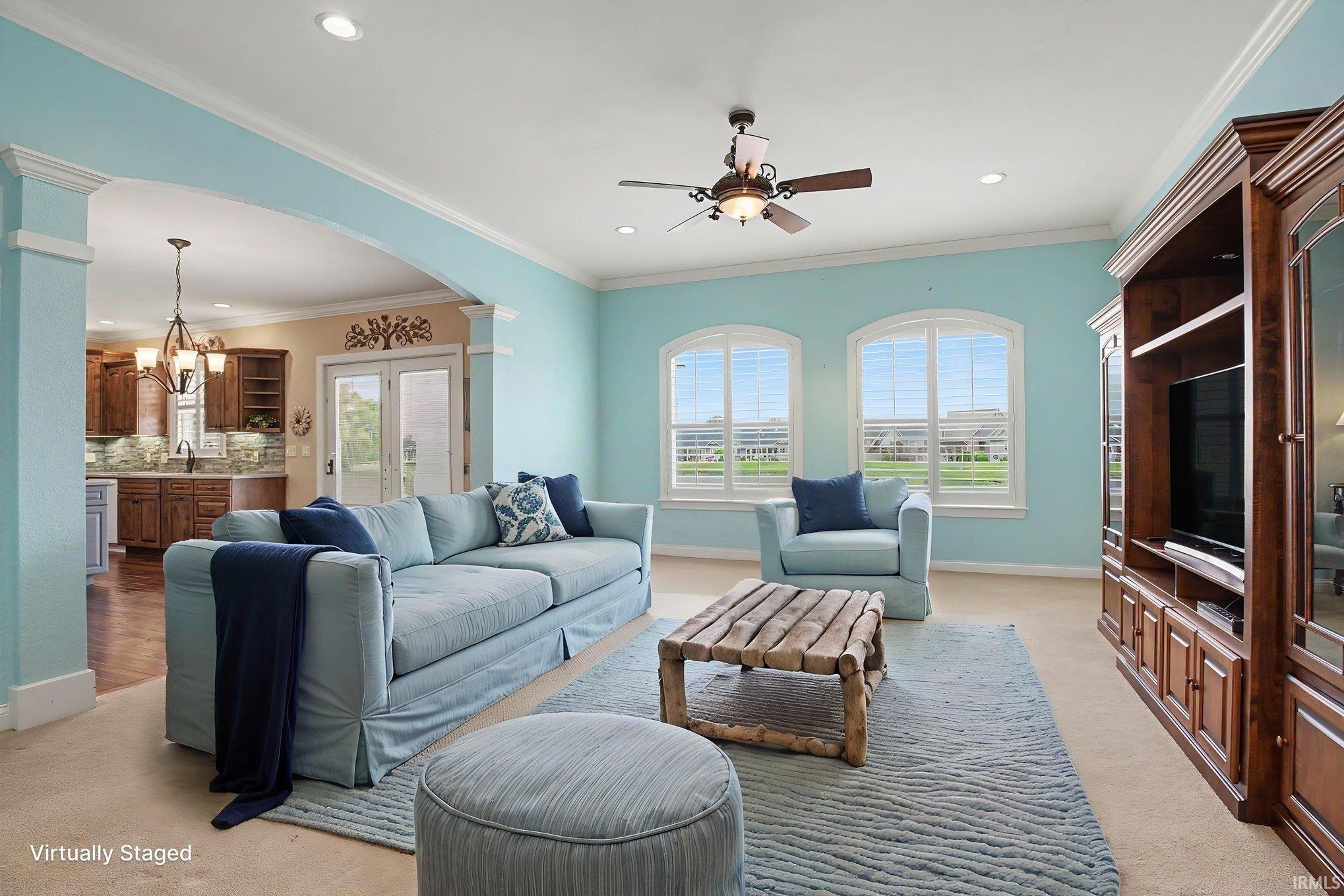 Living room featuring twin arched windows with plantation shutters, crown molding, a ceiling fan, and a built-in entertainment center