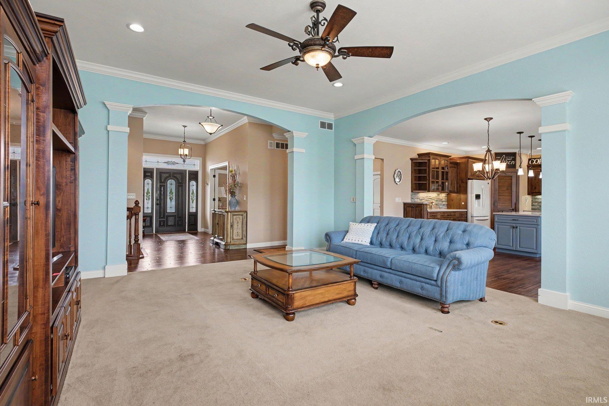 Carpeted living area featuring arched doorways, crown molding, and a ceiling fan with integrated lighting