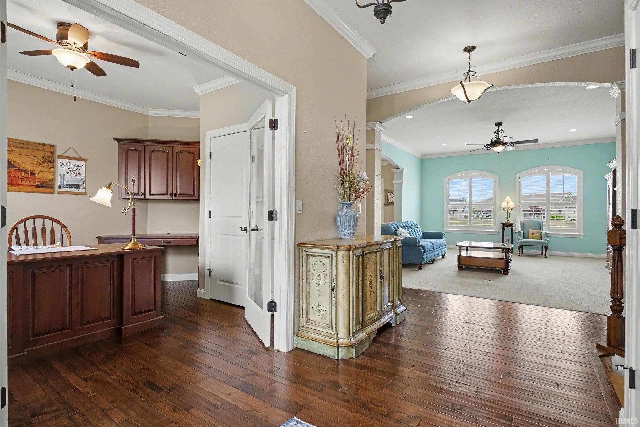 Hardwood flooring extending from the entryway into an office with built-in cabinetry and an adjoining room featuring arched architectural details and multiple arched windows
