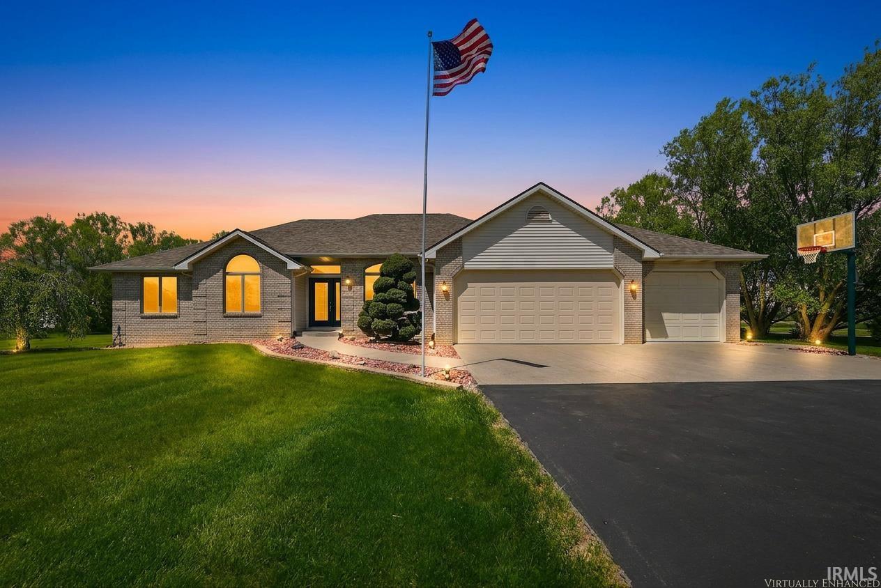 Ranch-style residence featuring a brick facade, attached three-car garage, expansive driveway, and manicured landscaping