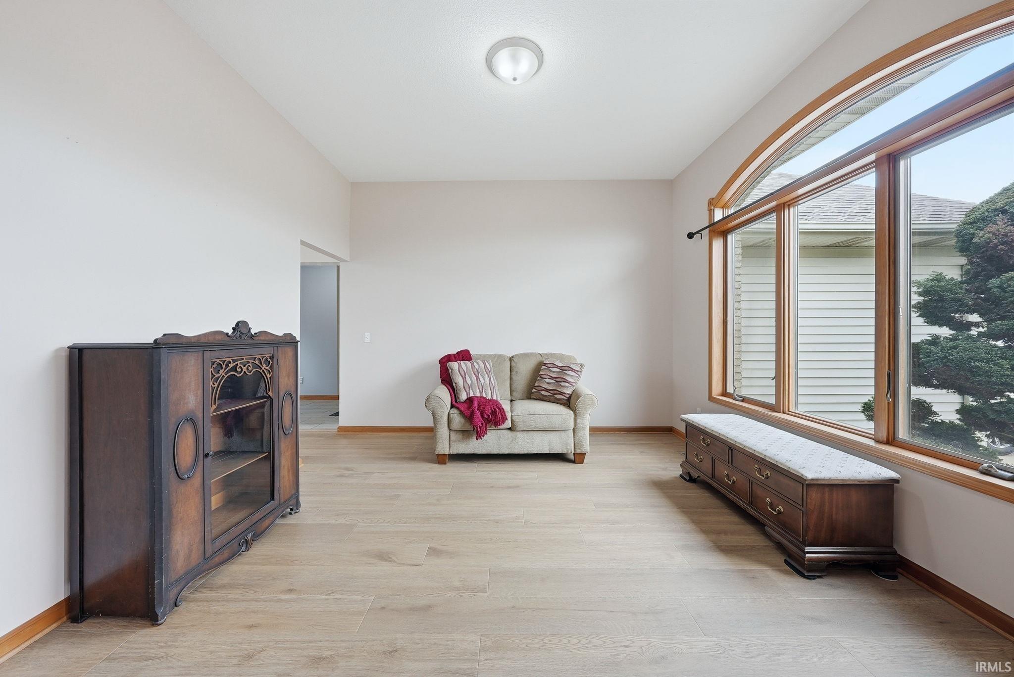 Expansive room featuring a large arched window with natural wood trim, wood-finish flooring, a neutral color palette, and a semi-flush mount ceiling light fixture
