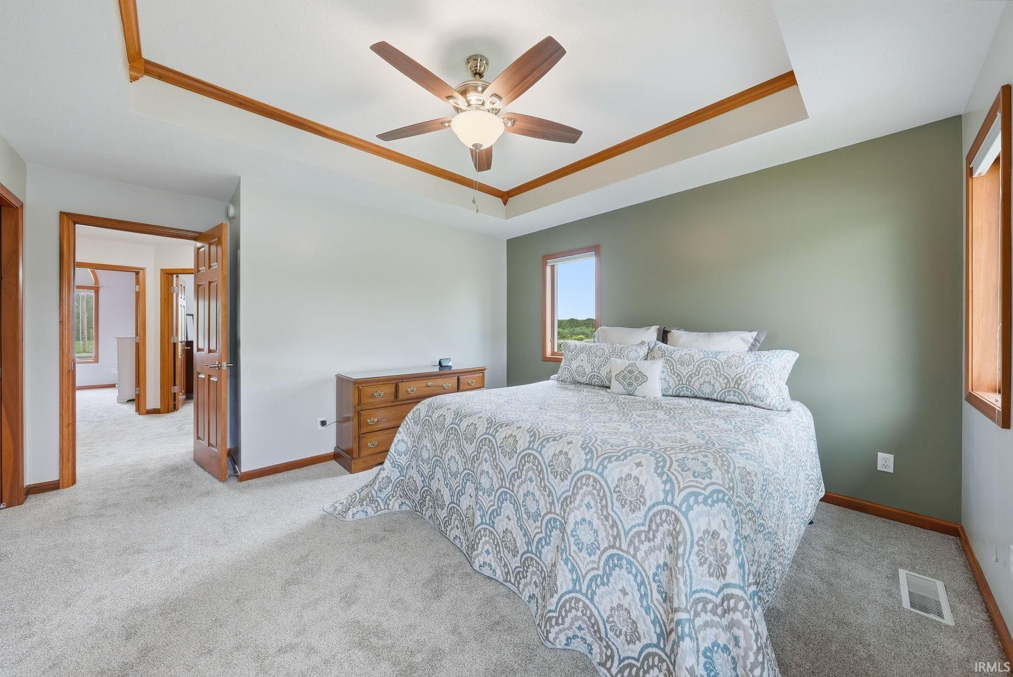 Bedroom featuring a tray ceiling with wood-finish trim, a ceiling fan with integrated lighting, and light gray carpeting