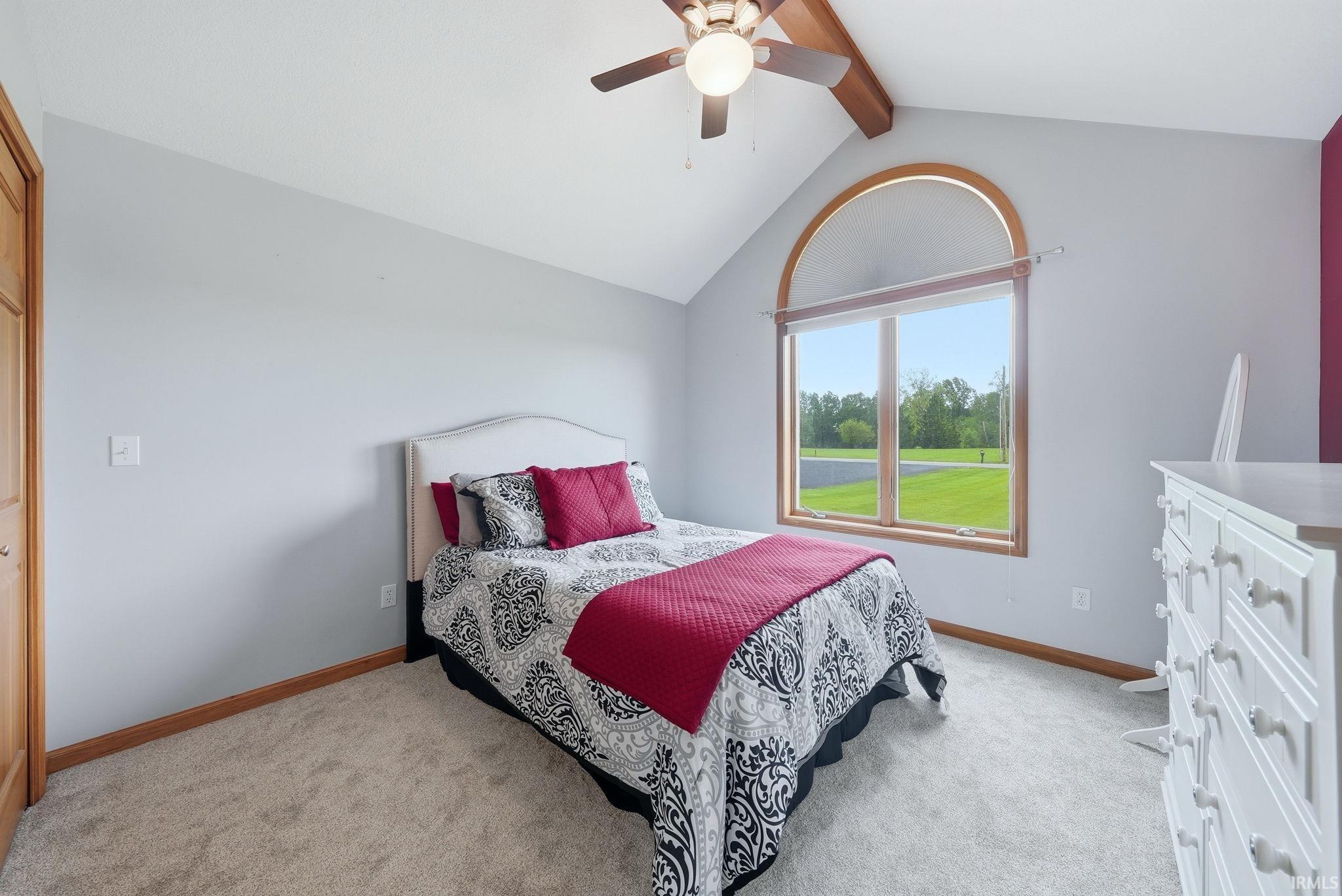 Vaulted ceiling with exposed wood beam, arched top window with wood trim, wood-finish flooring, and light-colored carpeting