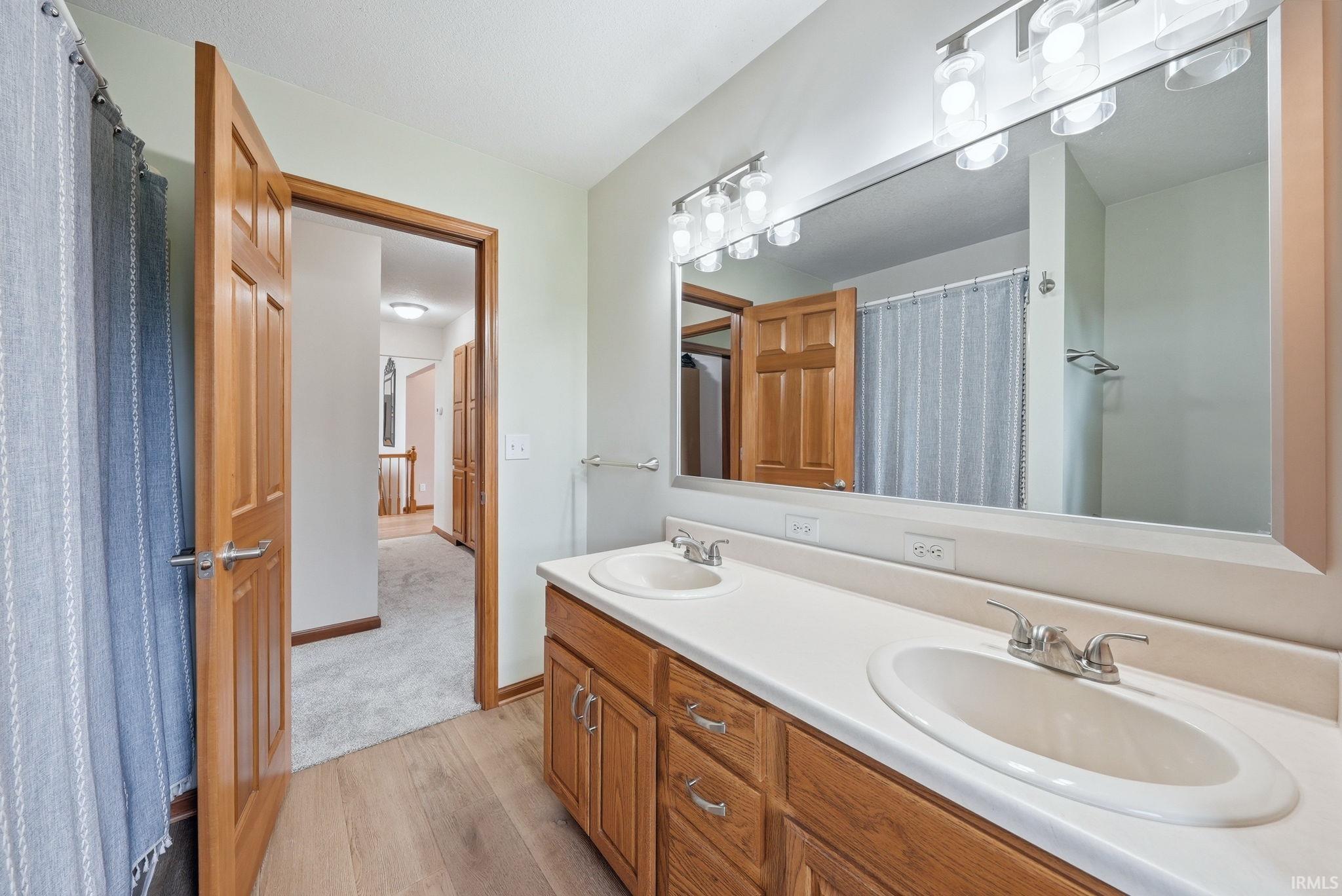 Double vanity with integrated sinks, wood-finish cabinetry, and a large mirror with overhead lighting