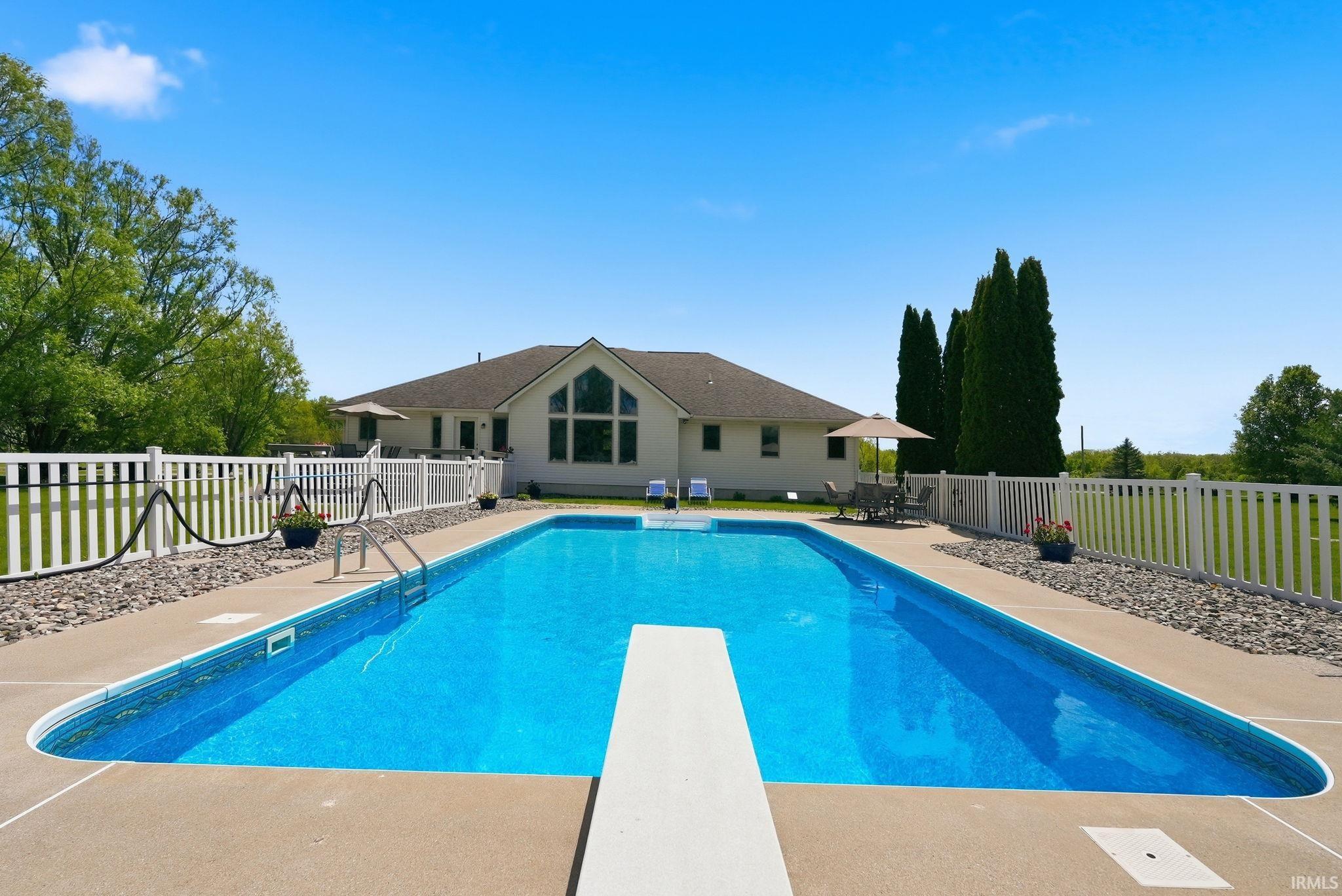 In-ground swimming pool featuring a diving board, surrounding concrete decking, and white picket fencing