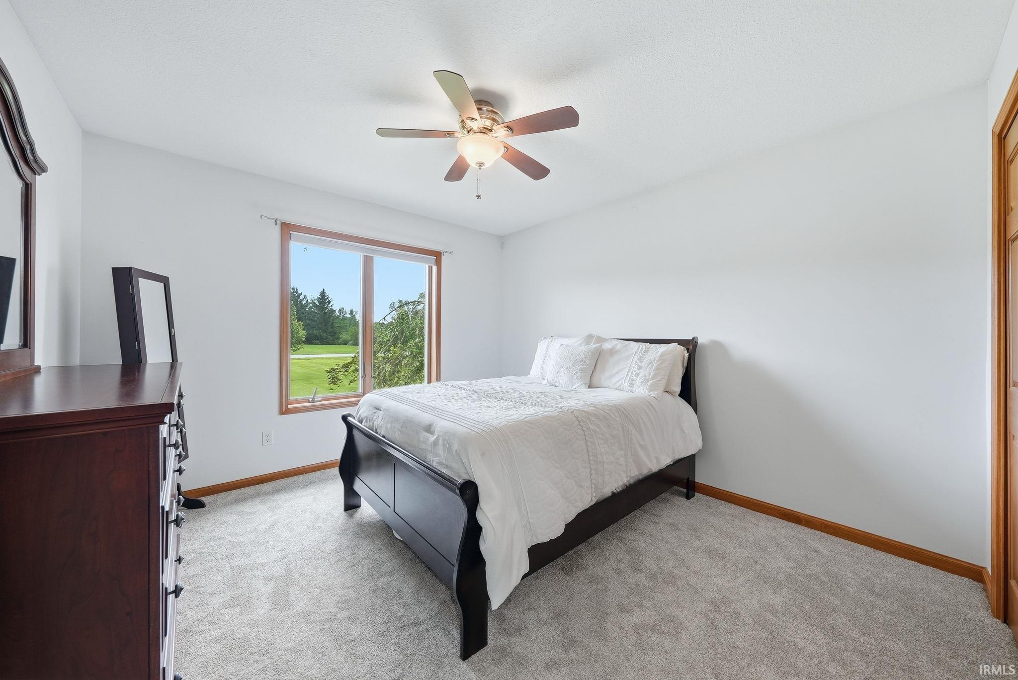 Room with light gray carpet flooring and white walls, featuring a window with wood trim overlooking a green landscape