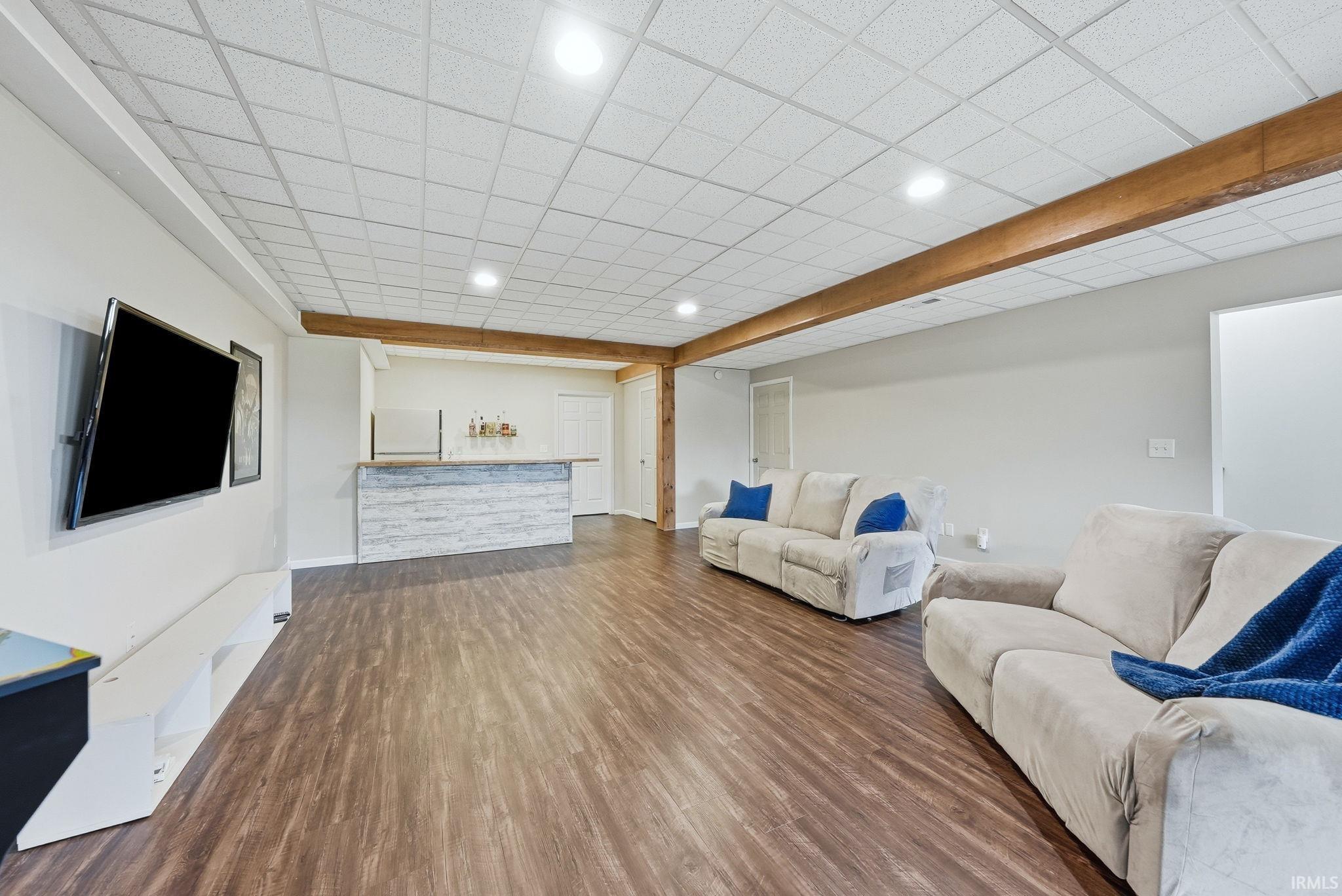 Finished basement featuring wood-finish flooring, drop ceiling with recessed lighting, and exposed wood beam accents