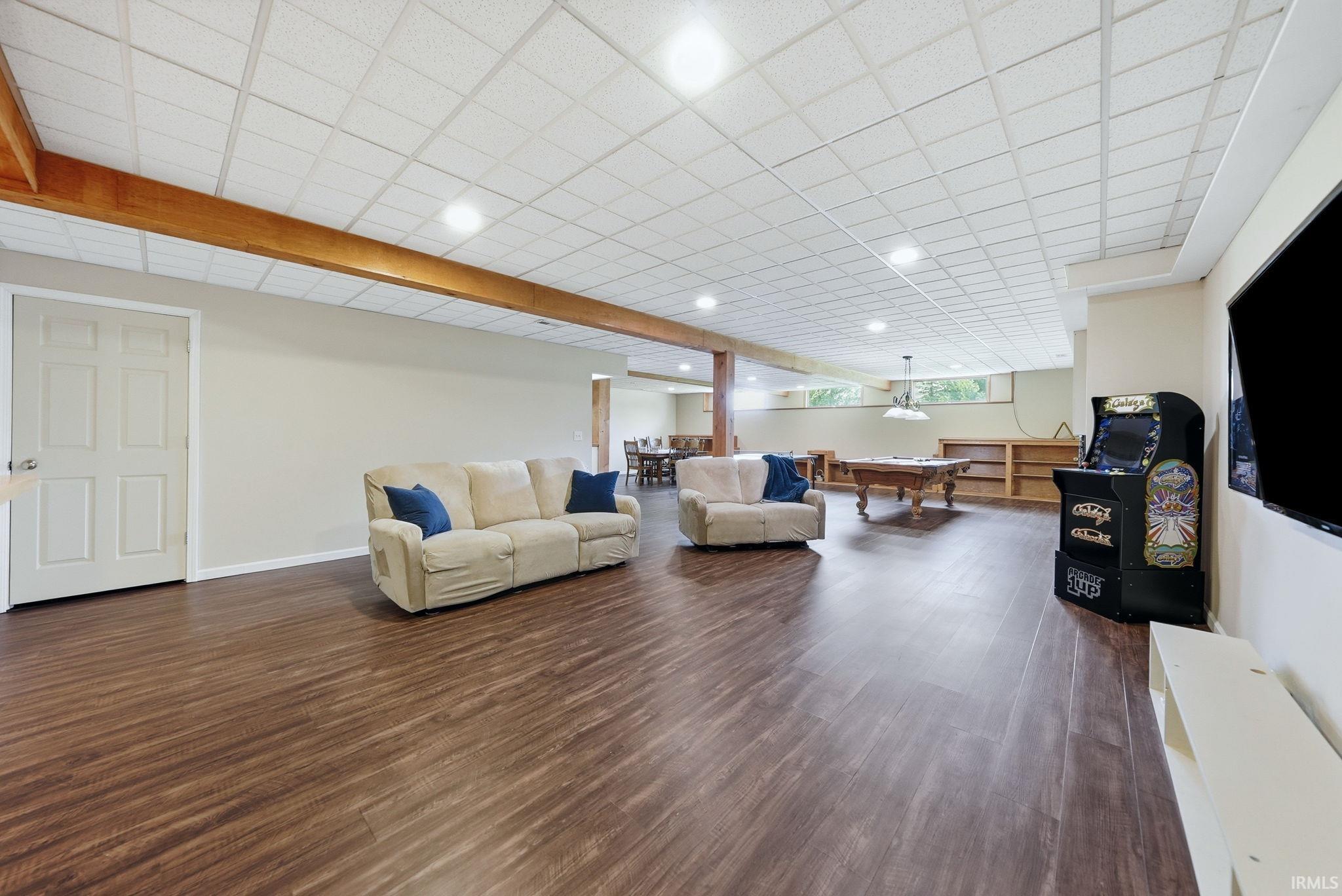 Spacious lower-level area featuring wood-finish flooring, recessed lighting, drop ceiling, light-toned walls, and a visible support beam