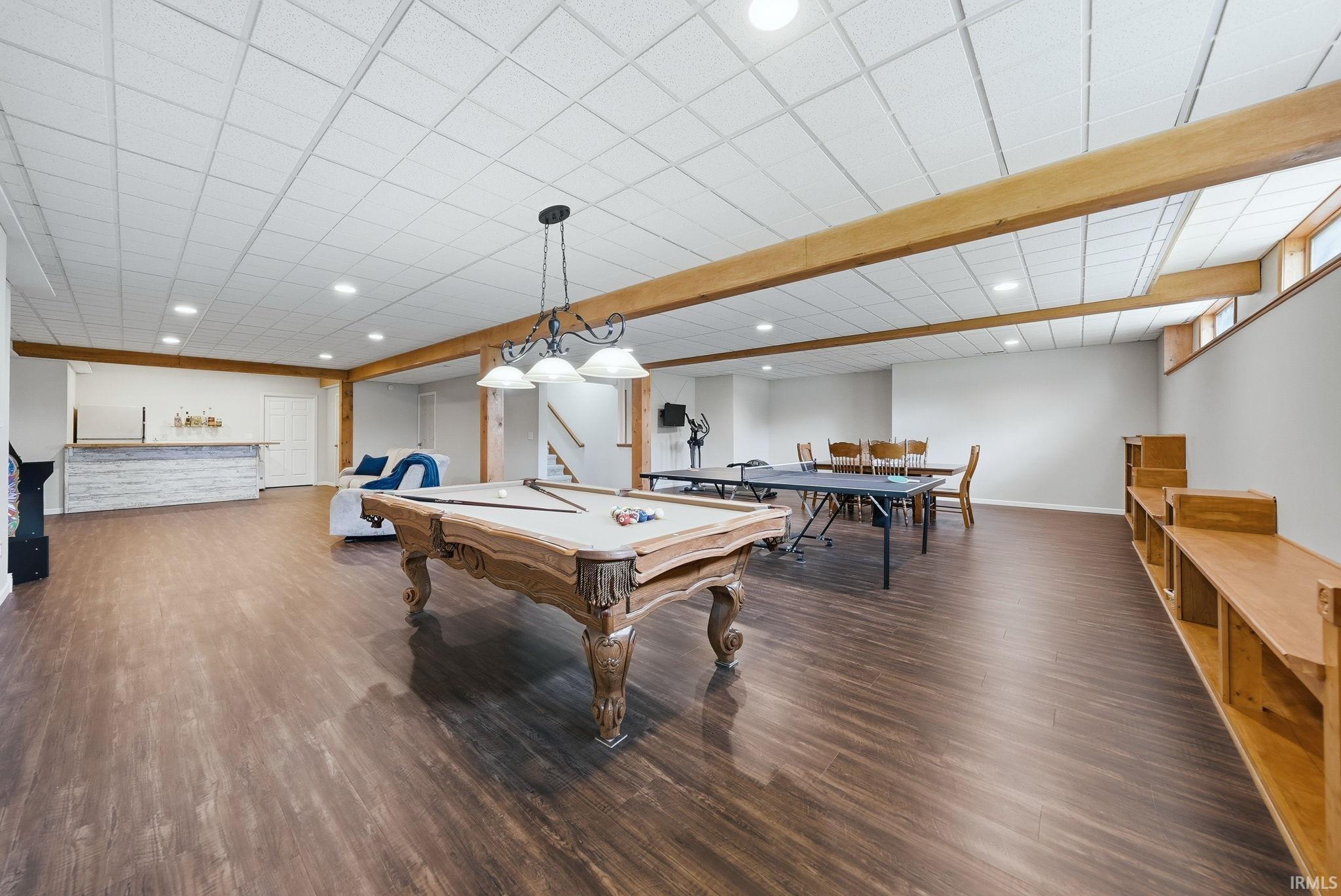 Expansive lower level featuring wood-finish flooring, a built-in wet bar with a shiplap facade, recessed lighting, and exposed wood ceiling beams
