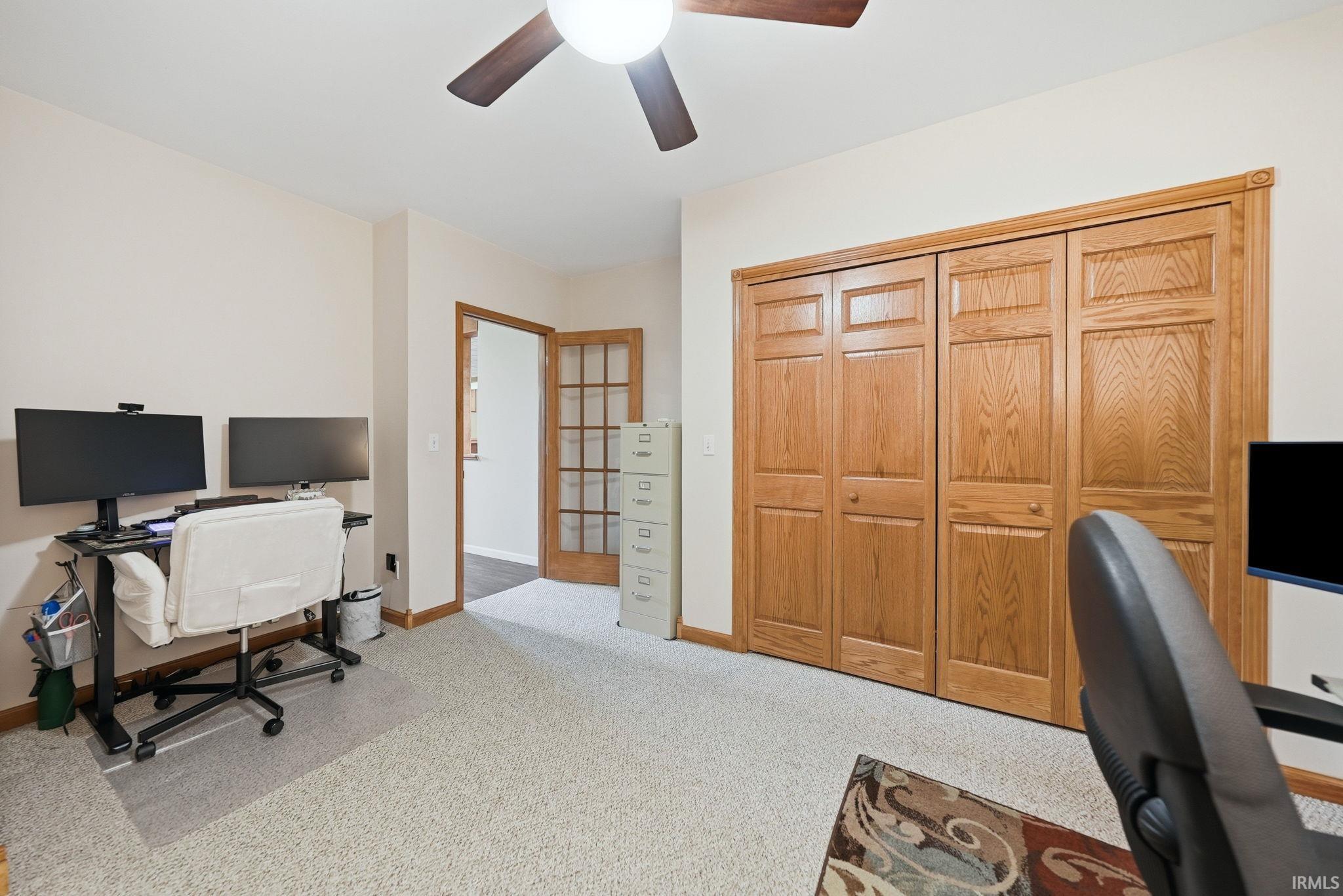 Room featuring light-colored carpeting, a ceiling fan with wood-finish blades, and warm-toned wood bi-fold closet doors
