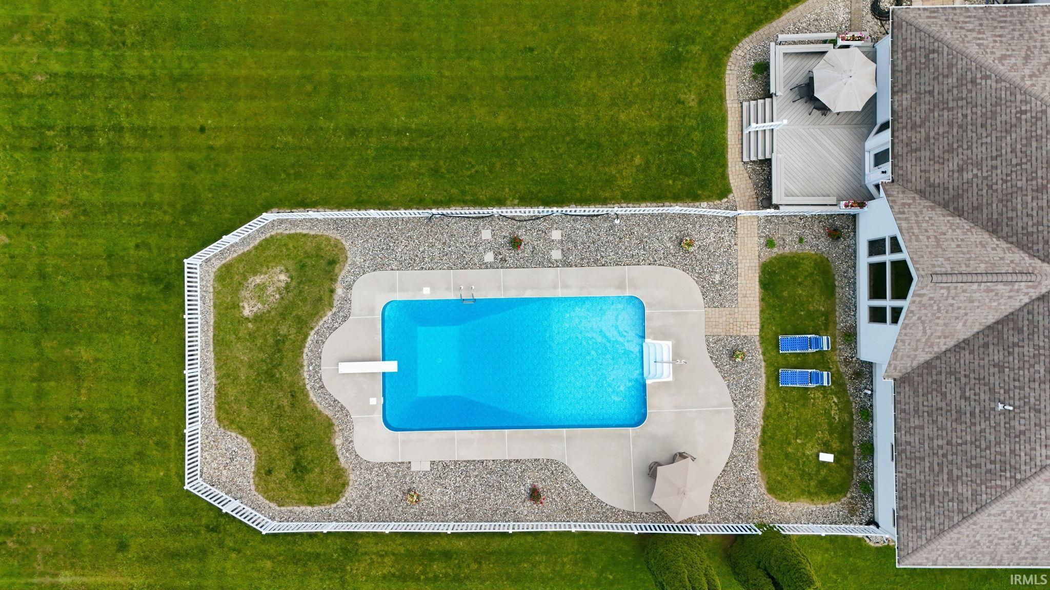 In-ground swimming pool with diving board, surrounded by a white picket fence and gravel landscaping