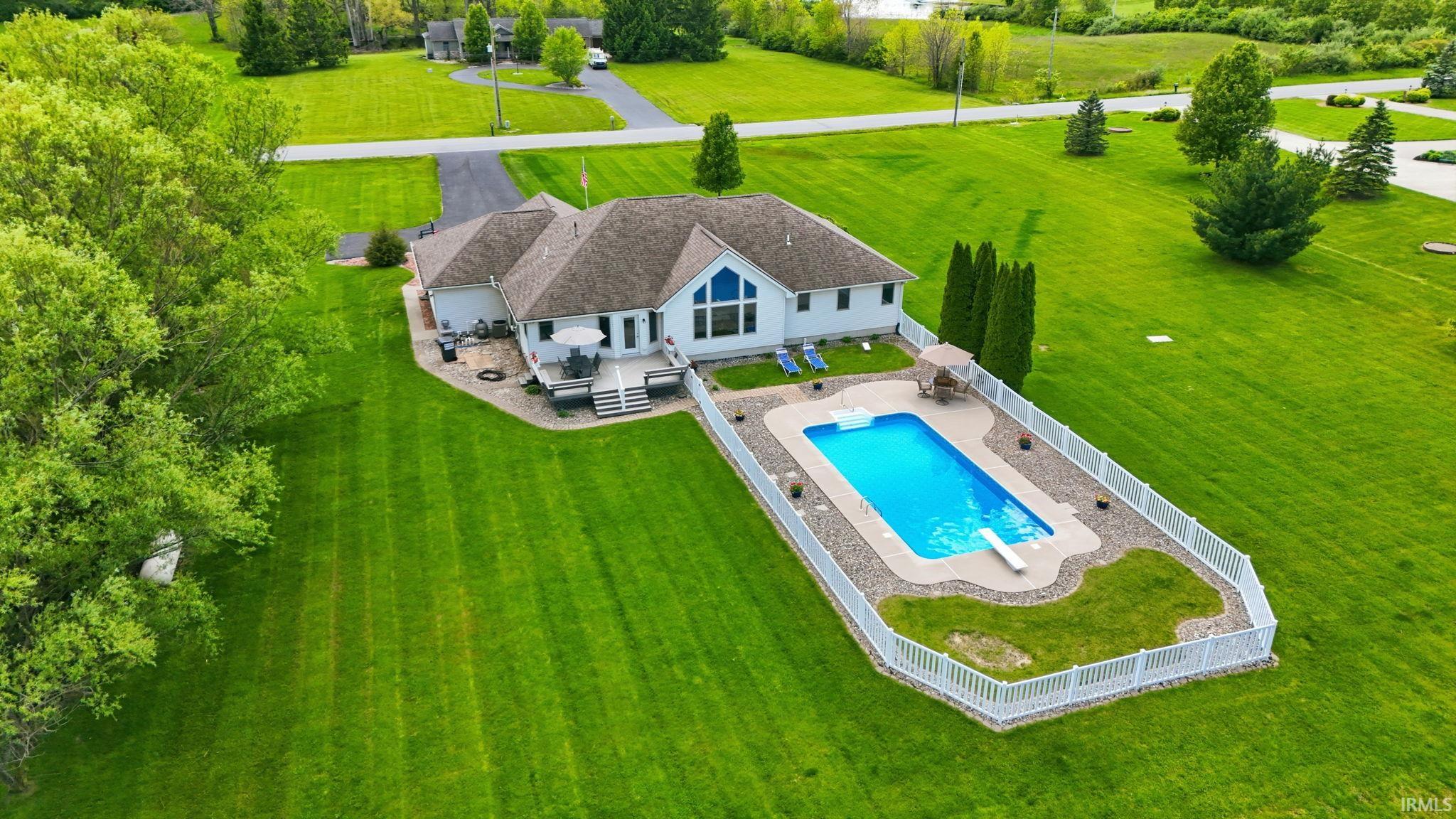 Expansive green lawn surrounds a single-story residence featuring a private pool area