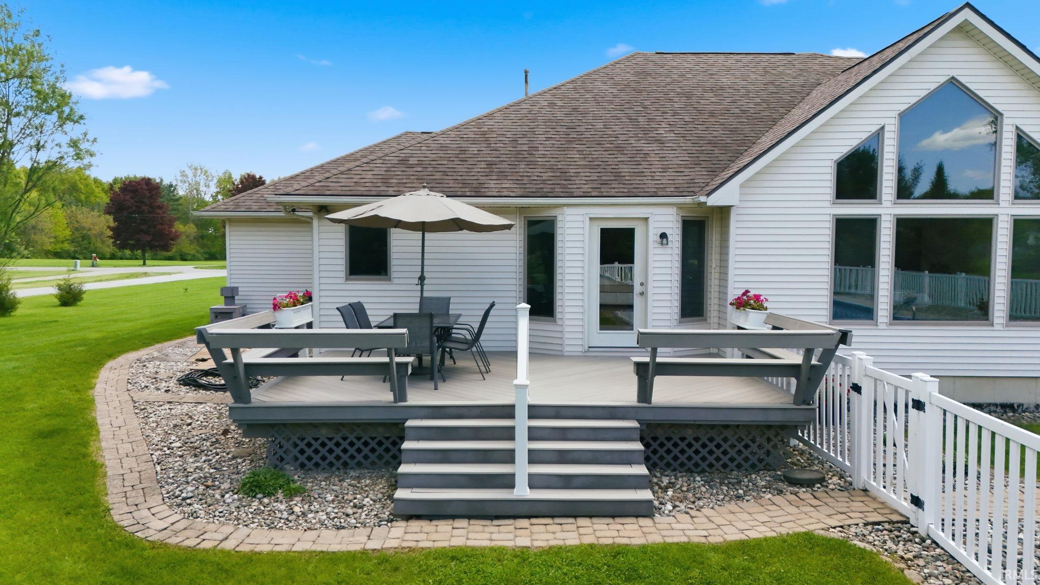 Exterior rear deck featuring composite decking, gray railing, and steps leading to a paver walkway