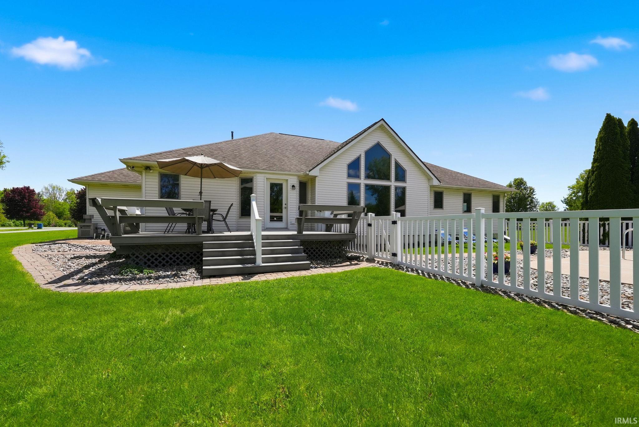 Expansive backyard featuring a manicured lawn, a multi-level deck with steps, a paver patio, a white picket fence, and a unique gable window design