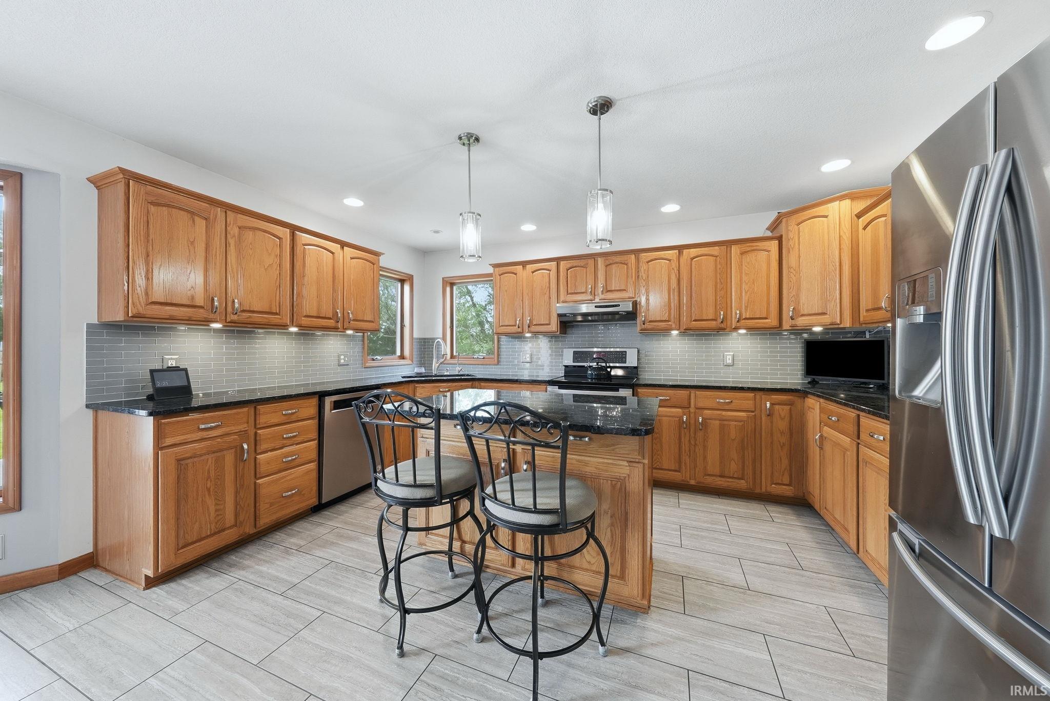 Kitchen featuring wood cabinetry, dark countertops, a tiled backsplash, stainless steel appliances, and large format tile flooring
