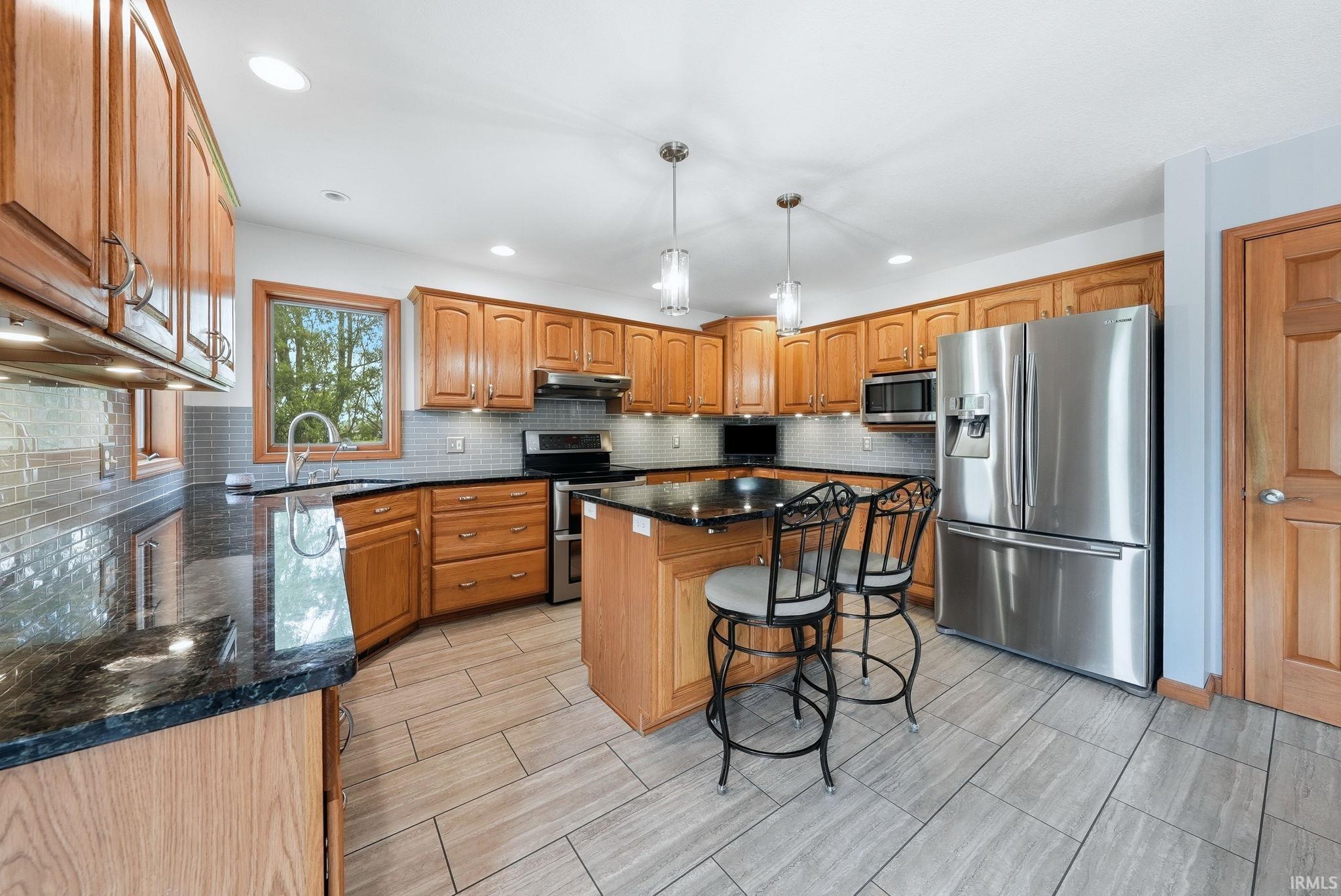 Kitchen featuring wood cabinetry, black countertops, tile backsplash, stainless steel appliances, and wood-finish flooring