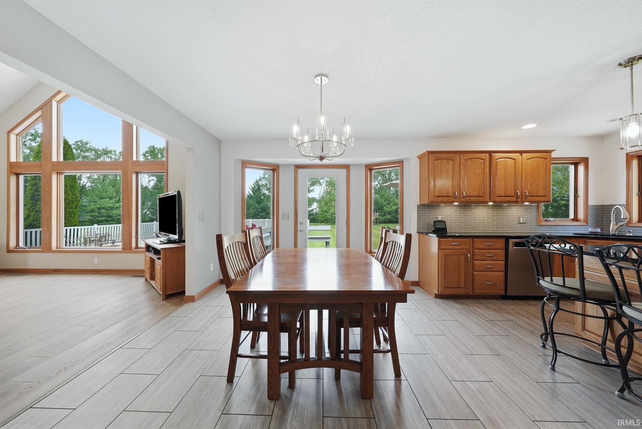 Open-concept interior featuring light wood-finish plank flooring, a kitchen with wood cabinetry and a tiled backsplash, and a dining area with a chandelier